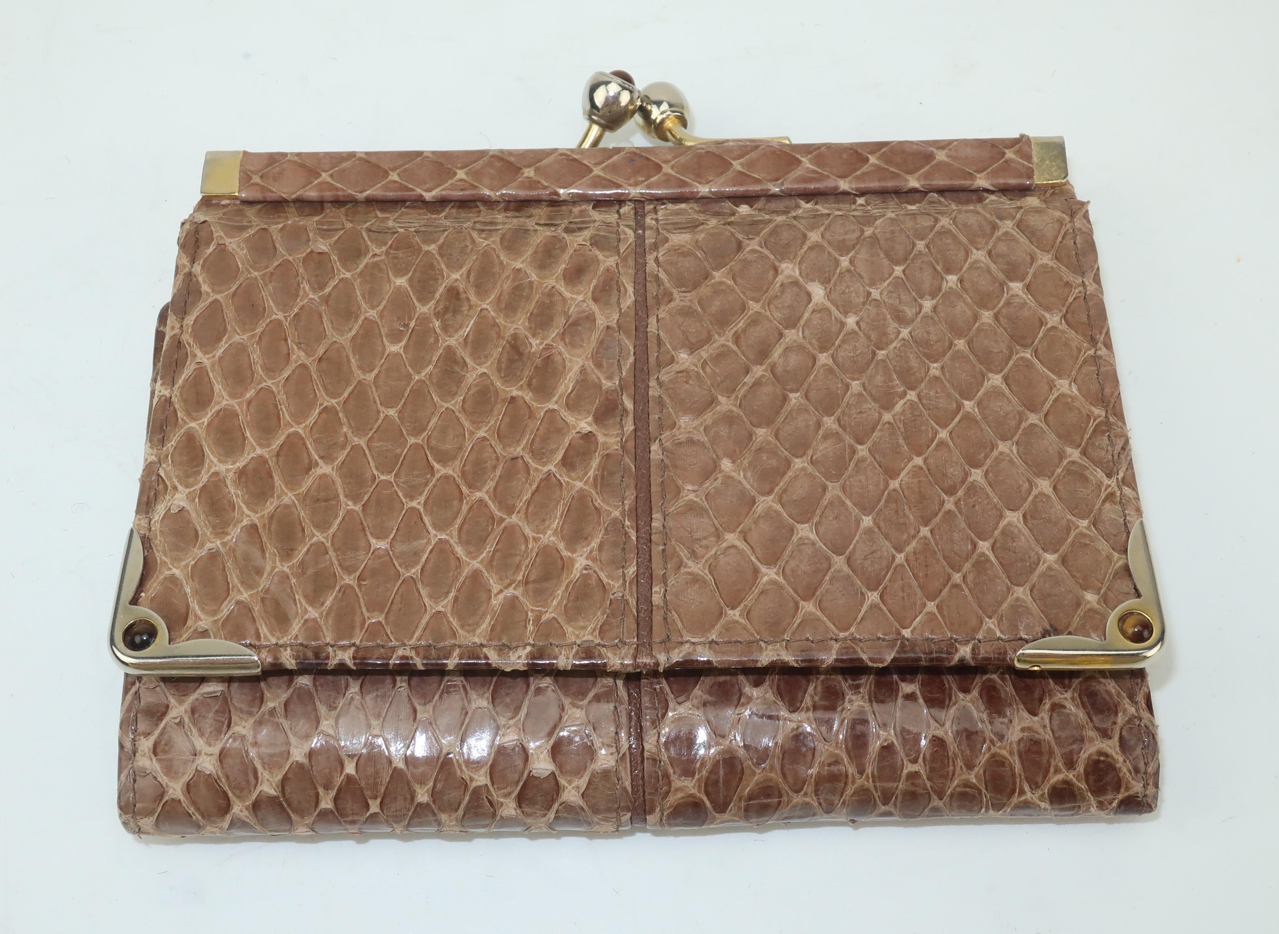 This small scale Judith Leiber taupe snakeskin wallet is a tri-fold design with gold tone corners and a kiss lock closure adorned with tiger’s eye stones.  The wallet snaps open to reveal a taupe leather interior featuring a large slot for bills and