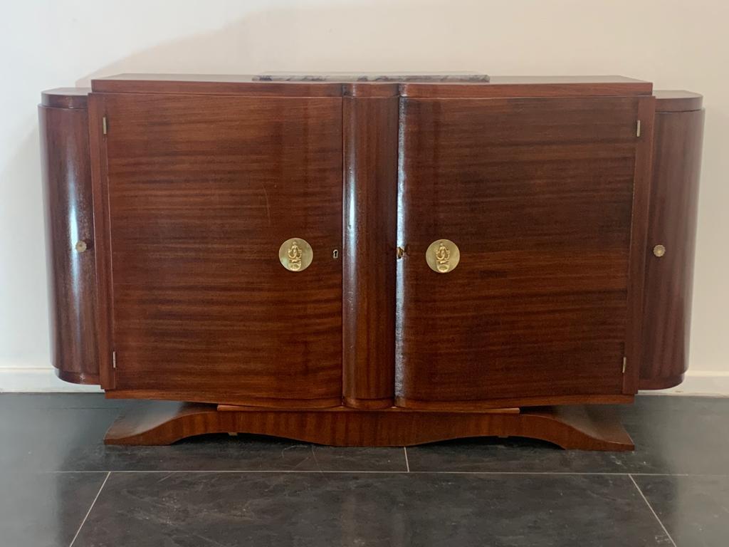 Art Deco sideboard in mahogany in the Jules Leleu style. Features 2 medallion handles with a two-tailed mermaid figure, 2 side knobs and gilt bronze hinges. On the recessed top a slab of gray marble veined with purple. Solid and functional