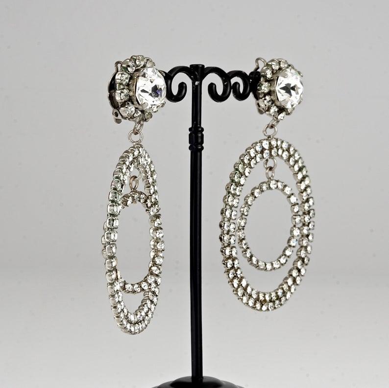 Vintage Jumbo CHANEL Double Hoop Orbital Rhinestone Dangling Earrings

Measurements:
Height: 3.54 inches (9 cm)
Diameter: 2.51 inches (6.4 cm)
Weight per Earring: 23 grams

Features:
- 100% Authentic CHANEL.
- Jumbo double hoop dangling earrings in