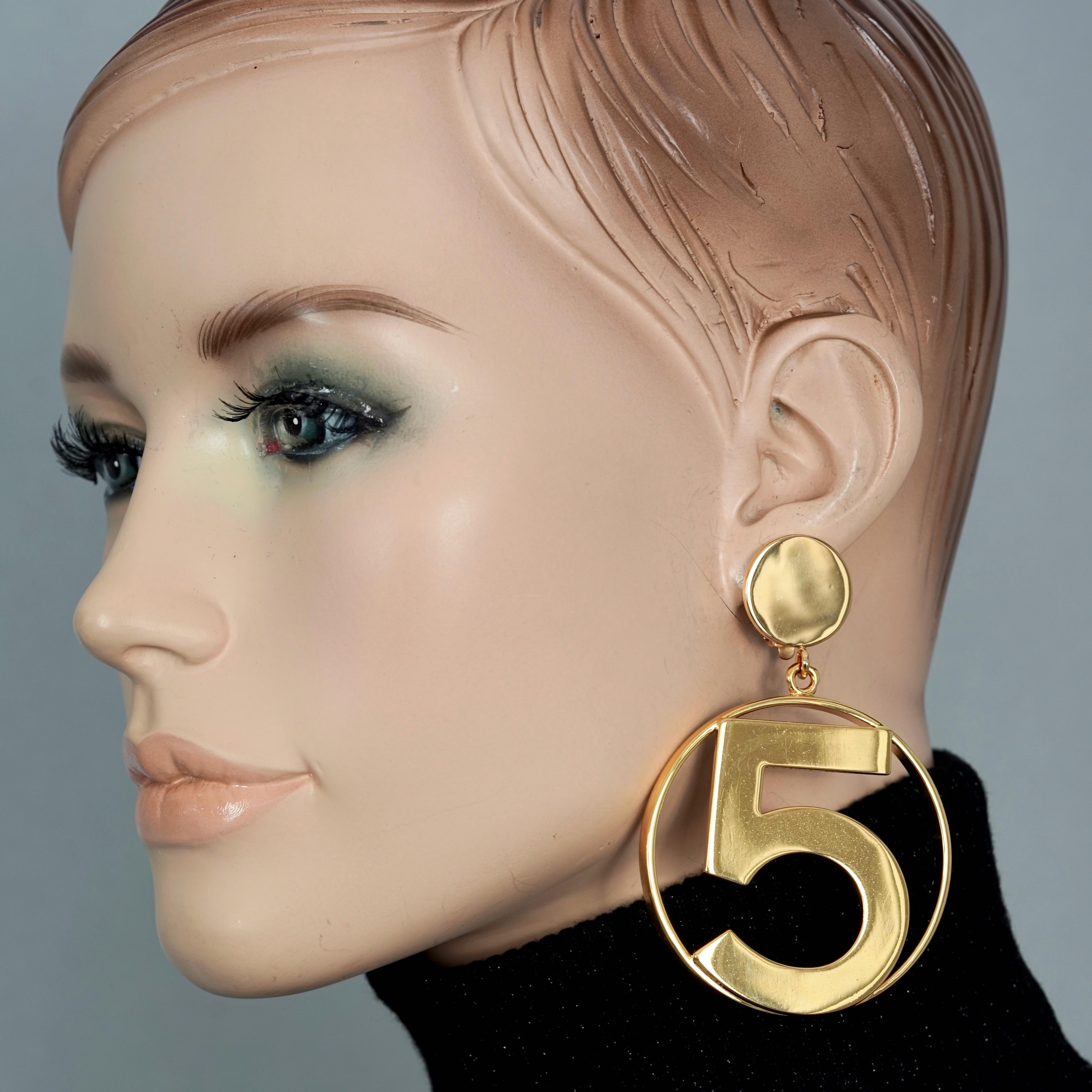Vintage Jumbo CHANEL Iconic No 5 Hoop Earrings

Measurements:
Height: 3.35 inches (8.5 cm)
Width: 2.20 inches (5.6 cm)
Weight per Earring: 35 grams

Features:
- 100% Authentic CHANEL.
- Iconic jumbo hoop earrings with No. 5 at the centre.
- Gold