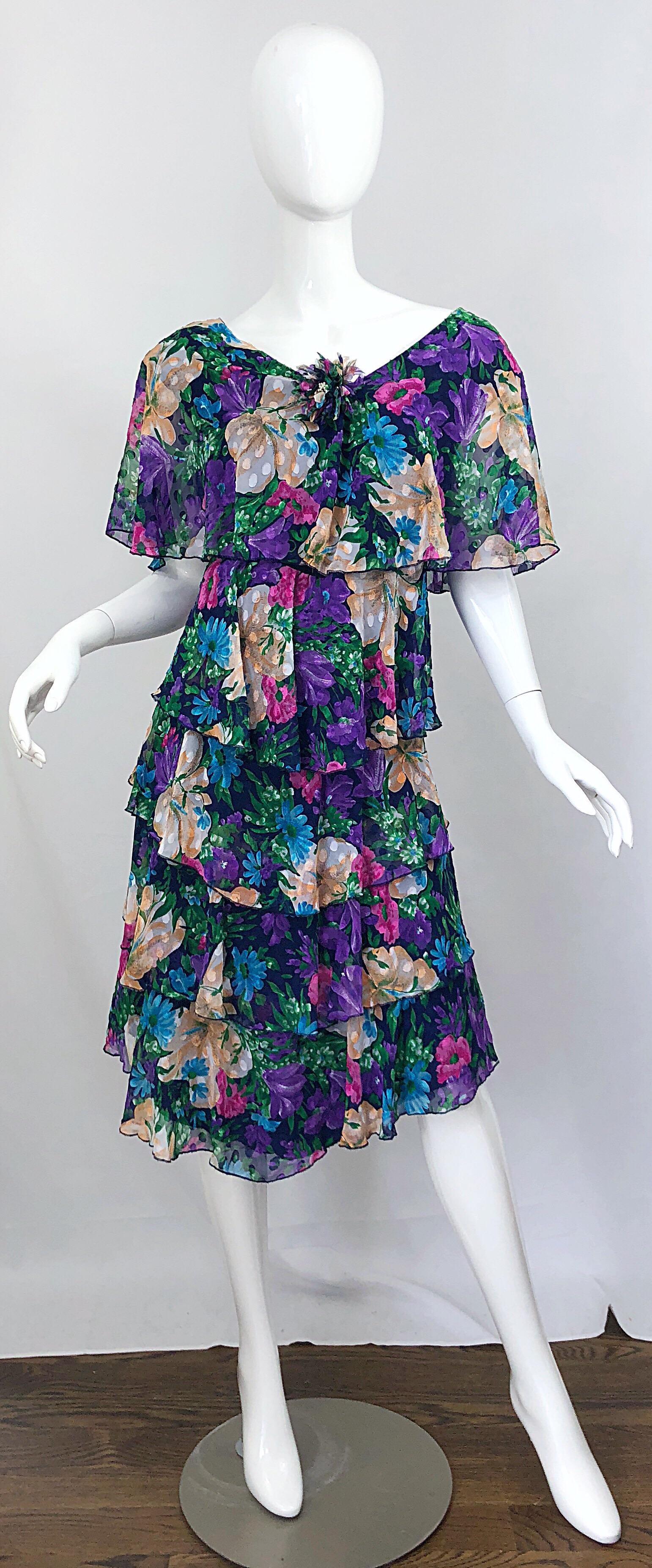 Beautiful 1980s JUSTIN DAVID floral chiffon larger size flapper style dress! Features flowers in vibrant colors of blue, turquoise teal, purple, pink, green, tan and white throughout. Flower brooch at center bust features dozens of tiny pearls, and