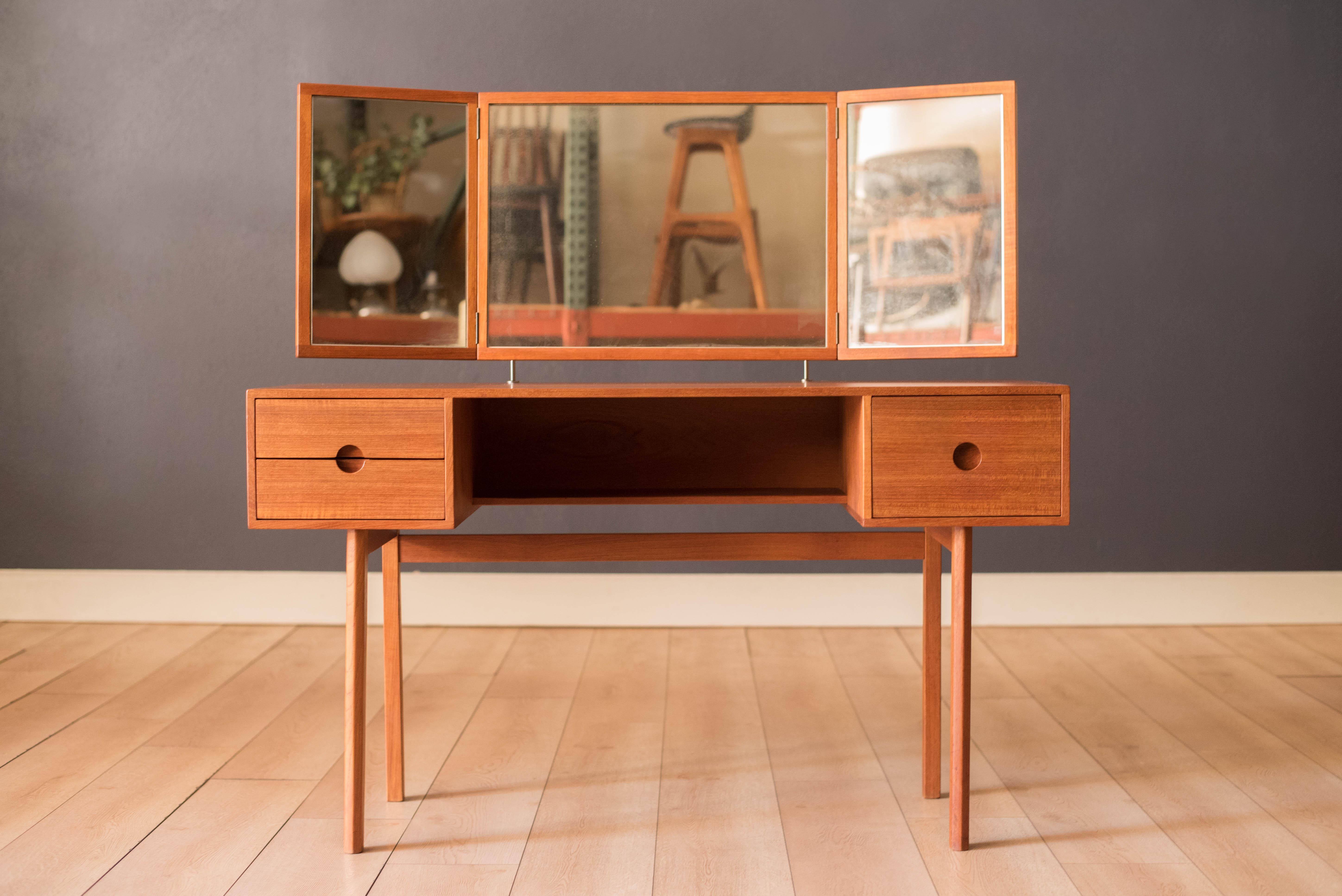 Mid Century Modern vanity dressing table in teak designed by Kai Kristiansen for Aksel Kjersgaard, Denmark. Features sleek circular recessed pulls that open three dovetail storage drawers and includes one center fixed shelf. The floating mirror is