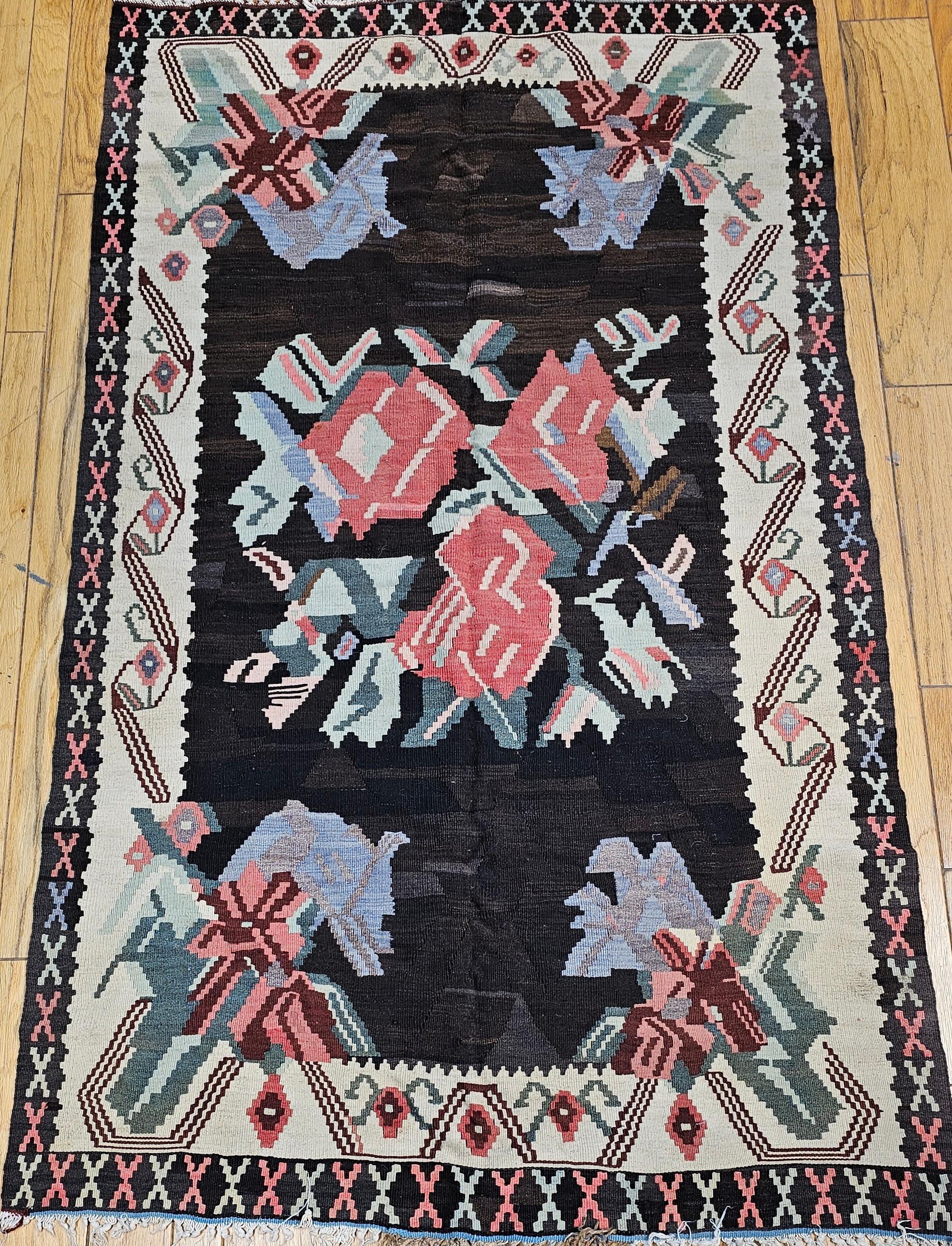 A vintage Karabagh  kilim with a single flower bouquet in the field and variations of flower designs in the four corners from the first half of the 1900s.  The field color is a combination of abrash black and brown with a border in cream color.  The
