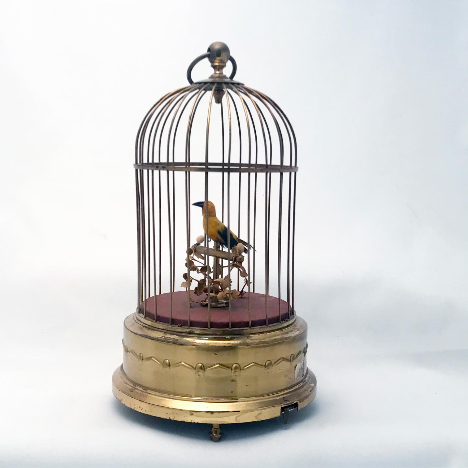 This bird is mainly yellow but with black wings, beak and tail feathers so is perhaps a canary. It cheeps tunefully and turns while doing so. The model retains its original leafy foliage, perch and brown ground. The brass cage is of the typical form