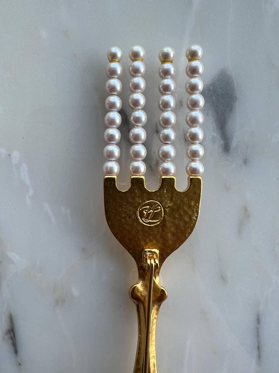 Broche Vintage By de Karl Lagerfeld représentant une fourchette avec des dents en fausses perles plaquées or 24k. 

Signé. Monogrammes KL. 

Période : 1990s

Condit : très bien. 

Longueur - 5.25