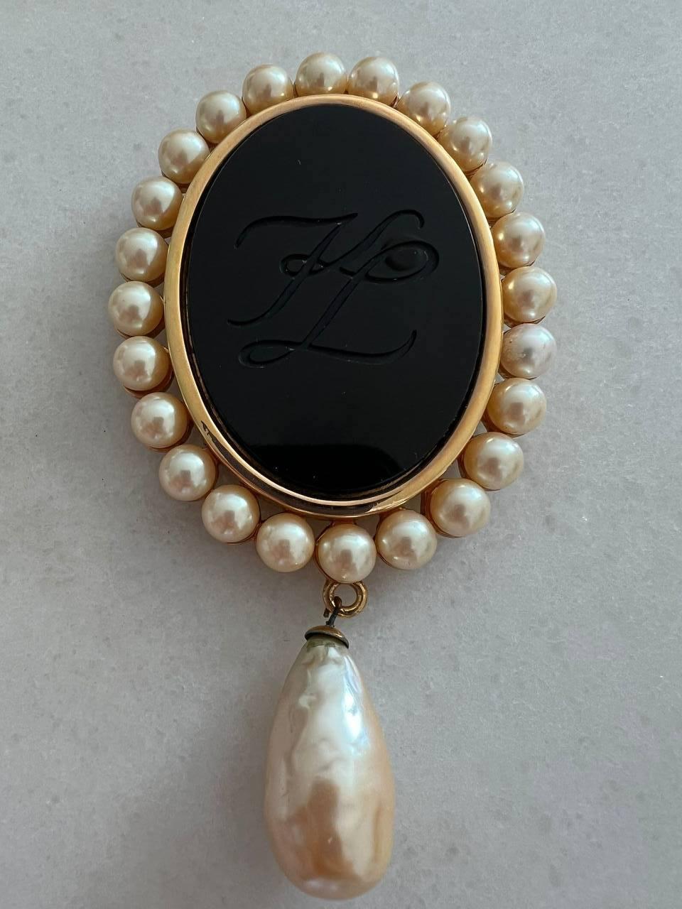 Vintage brooch black glass embossed with KL logo in gold-tone setting by Karl Lagerfeld. Accented with faux baroque pearls.
Signed. 
Period: 1990s
Dimensions: 
Length: 11,5 cm 
Width: 6,5 cm 
Condition: very good.

........Additional information