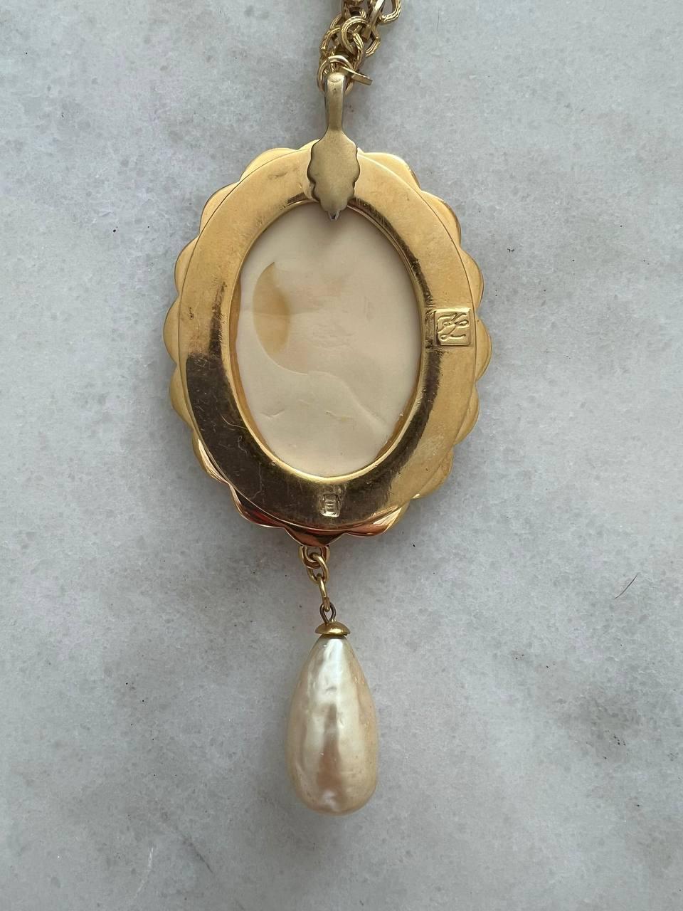 Vintage Necklace by Karl Lagerfeld featuring cream glass pendant embossed with KL logo in gold-tone setting. Accented with a faux baroque pearl.
Signed. 
Period: 1990s
Dimensions: 
Chain length: 75cm
Pendant length: 13cm 
Pendant width: 5,5 cm
