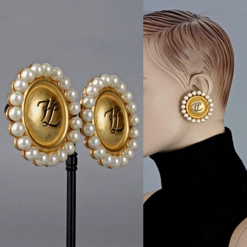 Vintage KARL LAGERFELD KL Logo Pearl Earrings

Measurements:
Height: 1.73 inches (4.4 cm)
Width: 1.73 inches (4.4 cm)
Weight per Earring: 24 grams

Features:
- 100% Authentic KARL LAGERFELD.
- Round earrings surrounded with faux pearls and KL logo