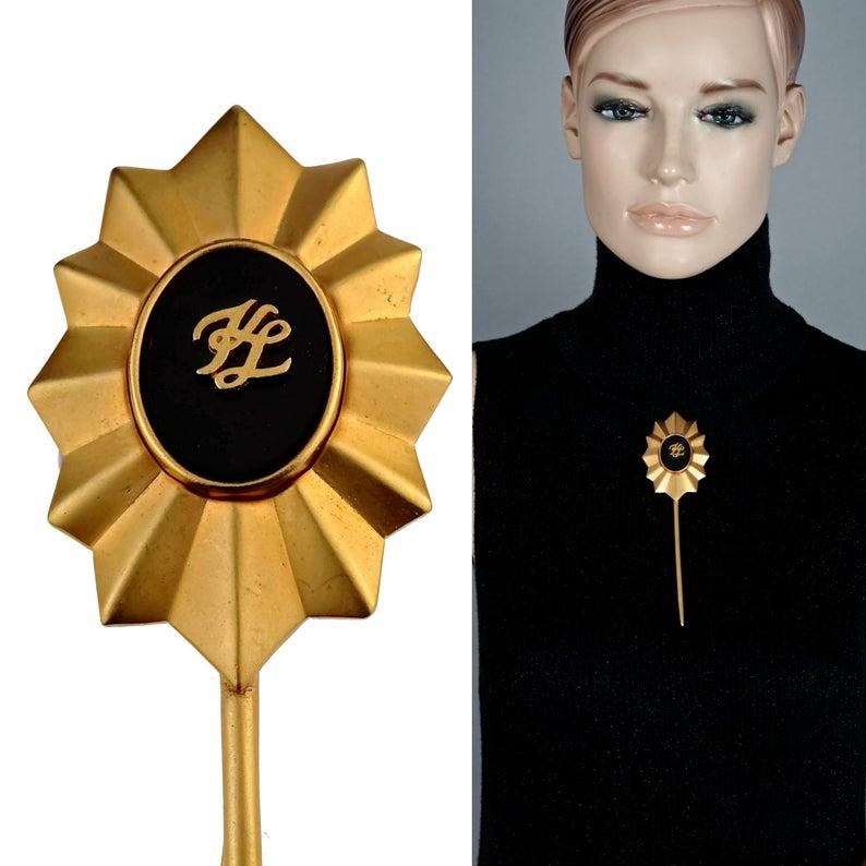Vintage KARL LAGERFELD KL Logo Sun Long Stick Brooch

Measurements:
Height: 2.12 inches (5.70 cm)
Width: 1.65 inches (4.2 cm)

Features:
- 100% Authentic KARL LAGERFELD.
- Sun motif long stick brooch.
- Matte gold tone hardware.
- Signed KL on