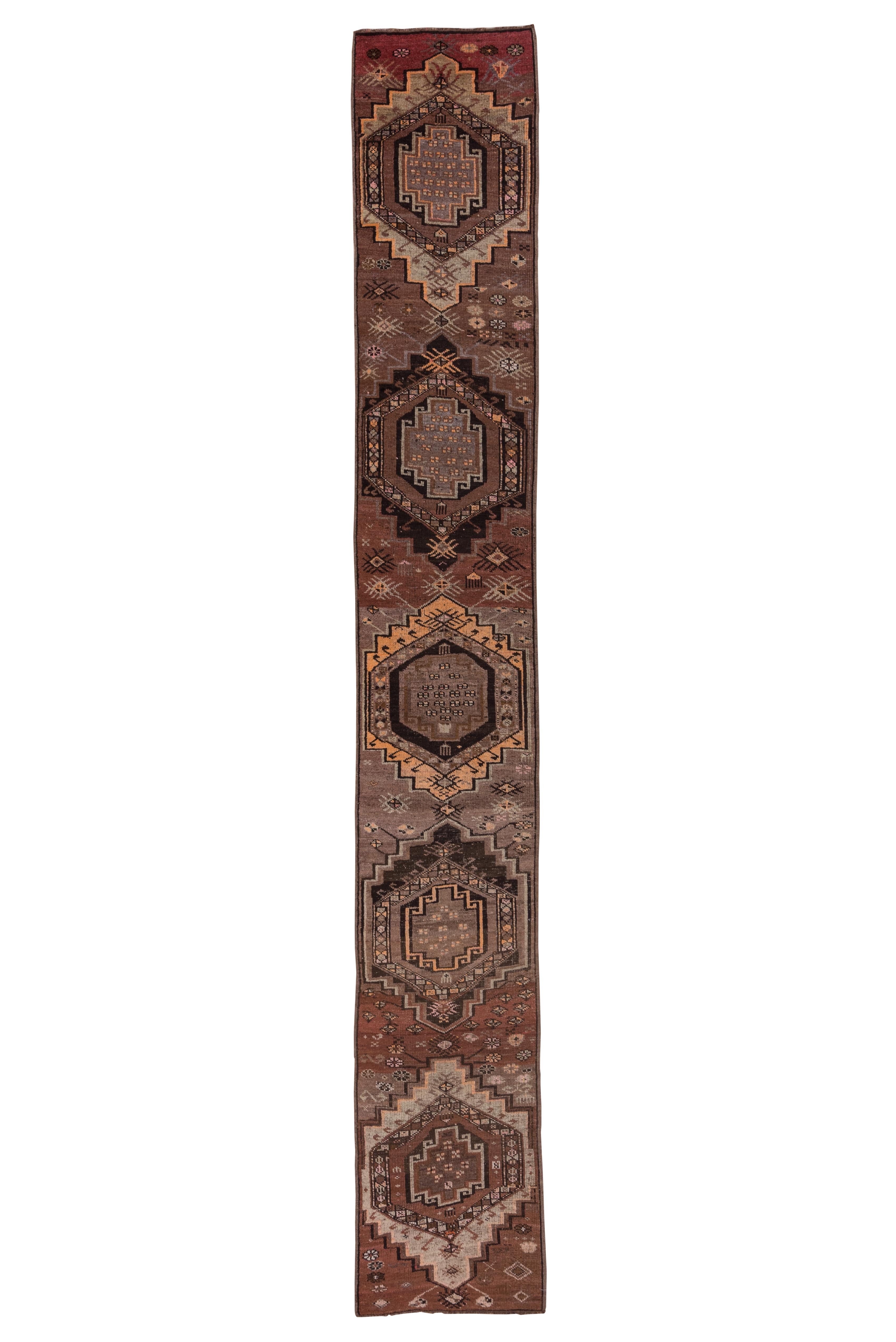 This coarse/moderate weave eastern Turkish runner shows a visibly abrashed coral field displaying four very large hooked and nested hexagonal medallions detailed in green, straw, coral, ecru and ruby. Secondary small rayed motives. Lacking borders