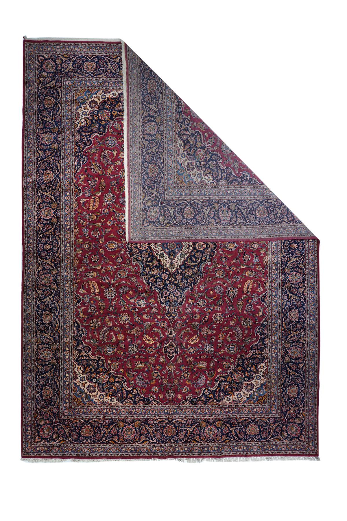 Vintage Kashan rug 10'4'' x 14'. This well-woven room size from a famous carpt-weaving centre, shows a blood red field closely hosting a variety of medium-scale palmettes, moving around the navy medallion with a small pattern and a cream