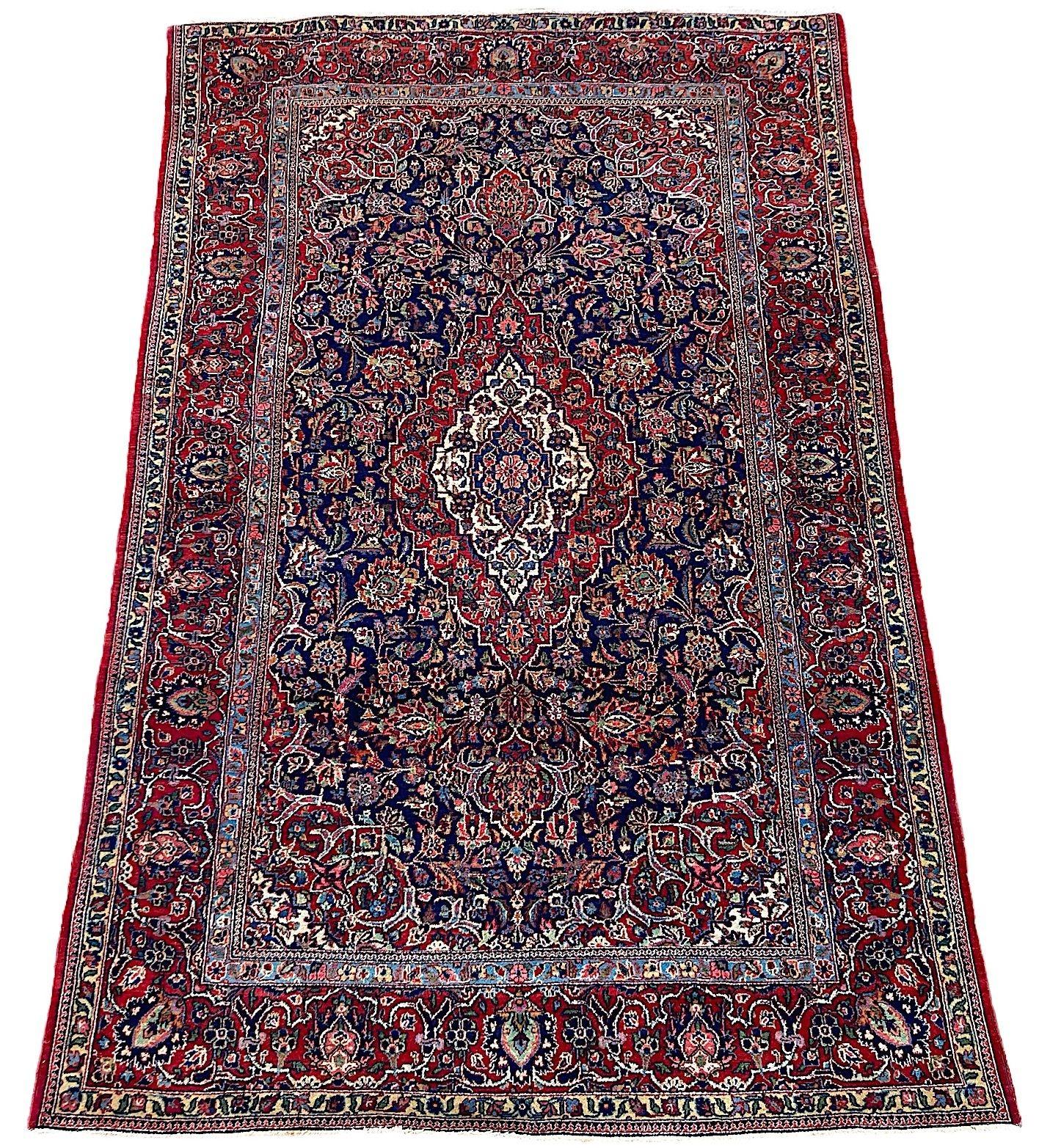 A lovely vintage Kashan rug, hand woven circa 1940. The rug features a classic Kashan design of a singular medallion on an indigo field of interconnected flowers and vines surrounded by a rich red border. Finely woven with lovely secondary
