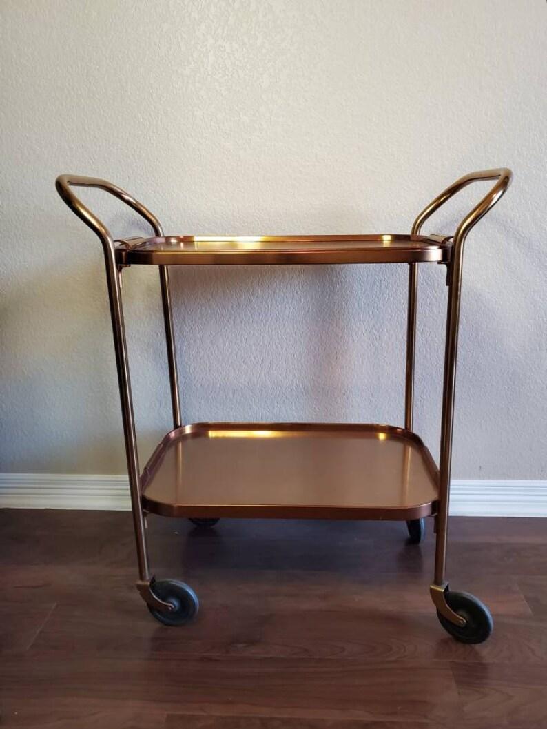 A stunning and rare mid-century modern aluminum serving bar cart / trolley by Kaymet. Born in England during the 1950s-1960s, having a removable tray top, over lower tier, on wheels. 

Gorgeous copper / bronze / rose gold hues depending on the