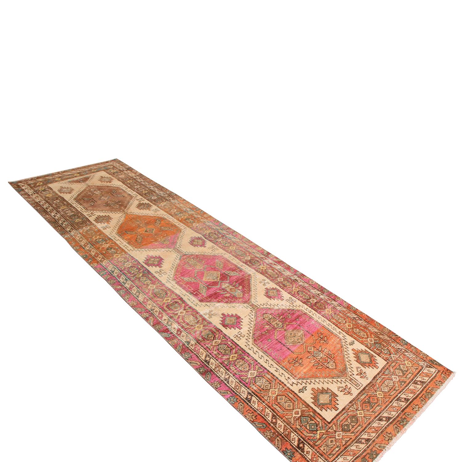 Originating from Pakistan in the 1950s, this vintage hand knotted wool Kazak runner enjoys one of the most distinguished and appealing marriages of rich and bright colorways, pairing autumnal and agricultural hues of beige-brown and tangerine red