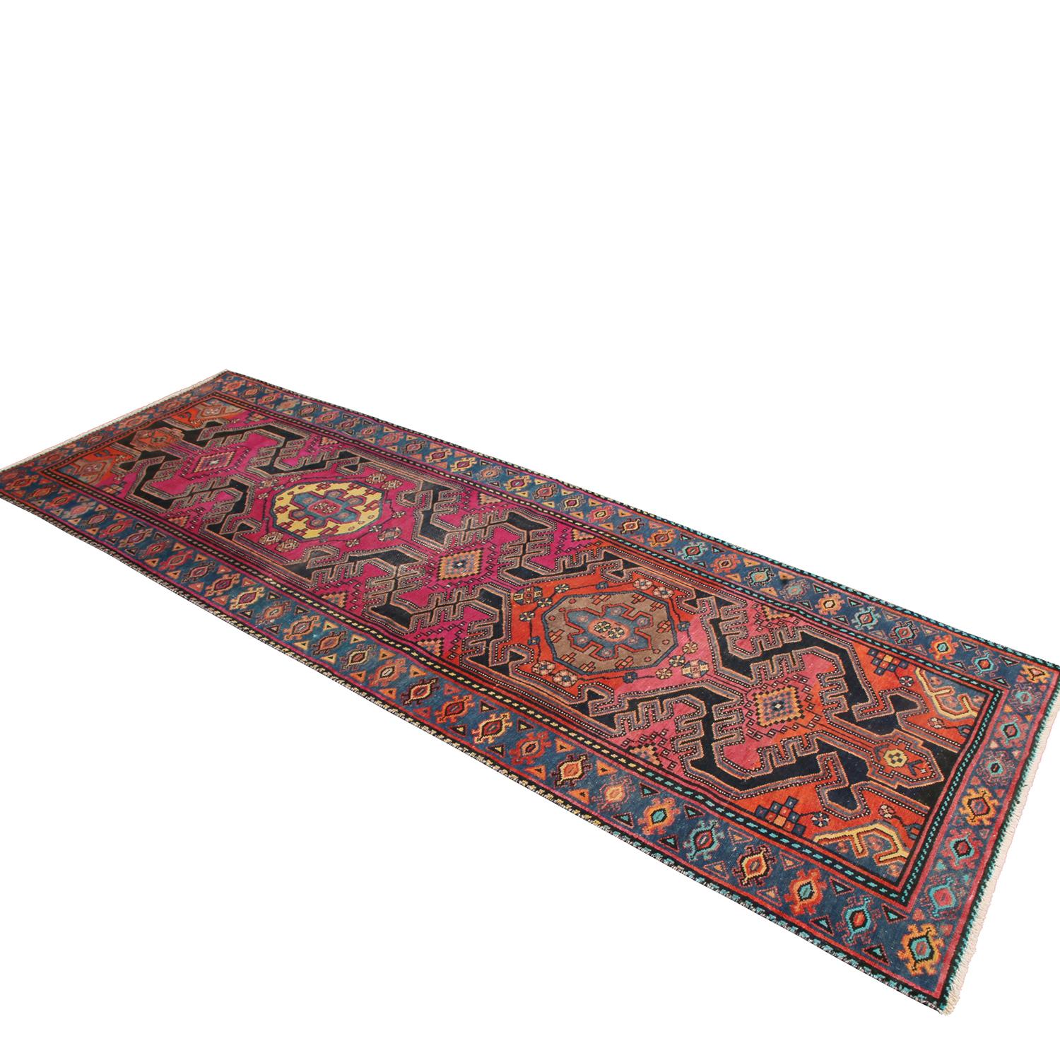 Originating from Pakistan in the 1950s, this vintage Kazak wool runner celebrates a distinct pairing of its navy blue border and background with the vivid magenta and red colorways dressing its field; both complementing the intricate, dimensionally