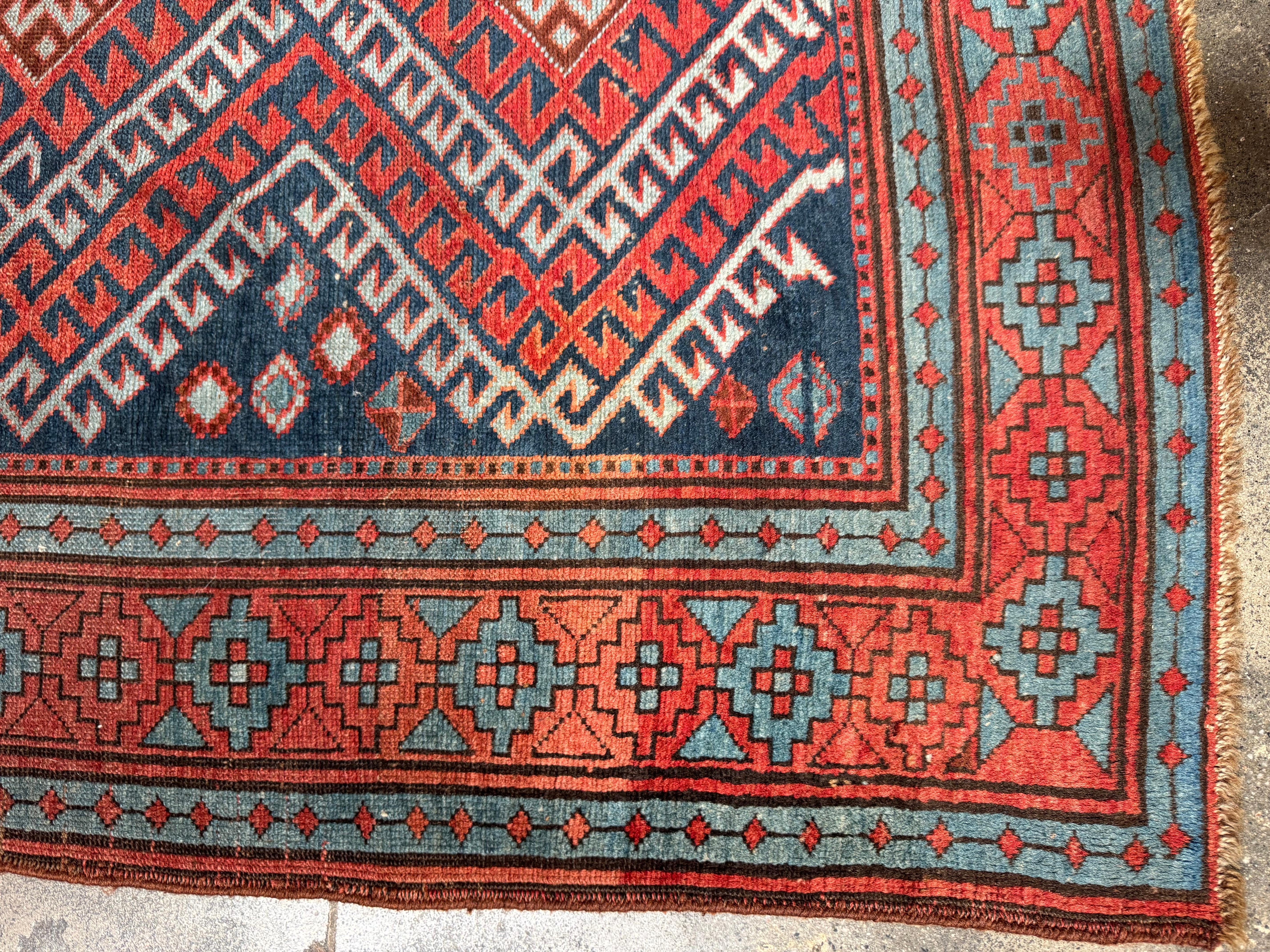 This striking vintage Kazak rug showcases a bold series of diamond medallions rendered in rich reds, icy blues, and earthy browns, layered over a dark navy field. The stepped motifs and lightning-like angles reflect classic Caucasian tribal design,
