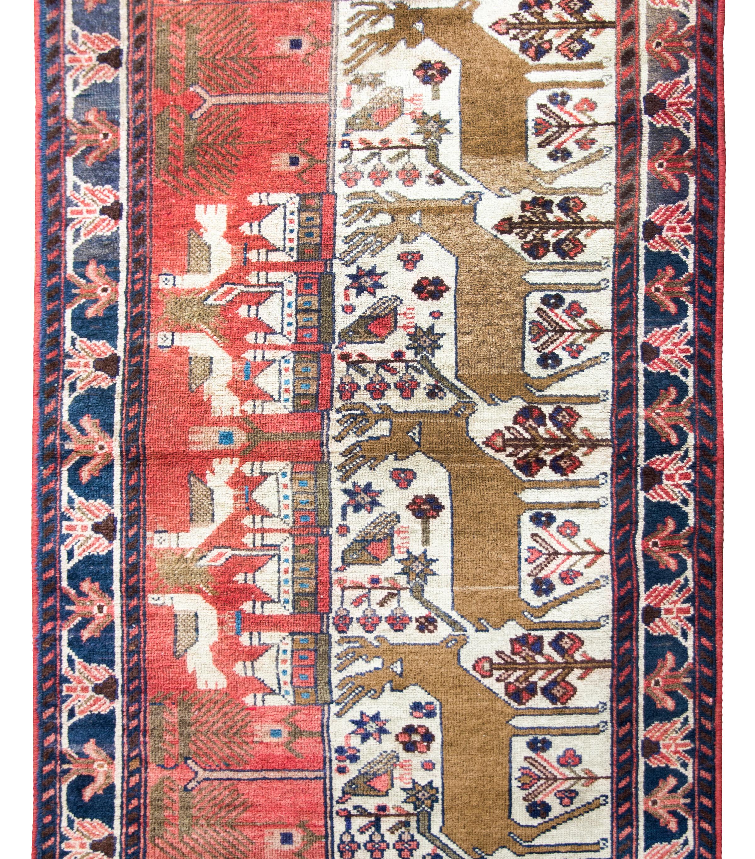 An incredible folky mid-20th century Persian Klederdasht pictorial rug depicting four large deer living amidst a field of flowers, with a village in the background, and four large doves above.  The border is simple, with a repeated floral pattern