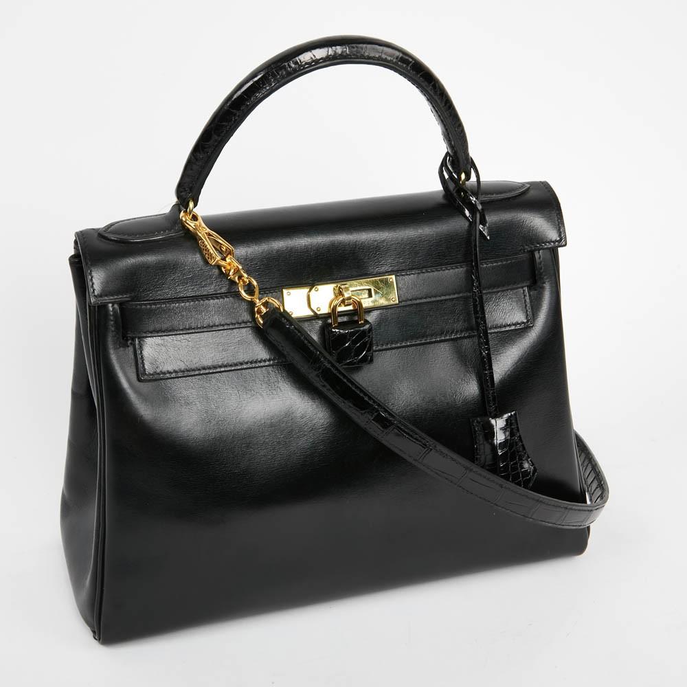 A must-have Kelly 28 bag from Maison Hermès, in a black box leather and alligator. It is worn by hand or shoulder by a removable shoulder strap. The lining is black with 3 pockets, one with zipper. The hardware is golden brass (micro scratches). It