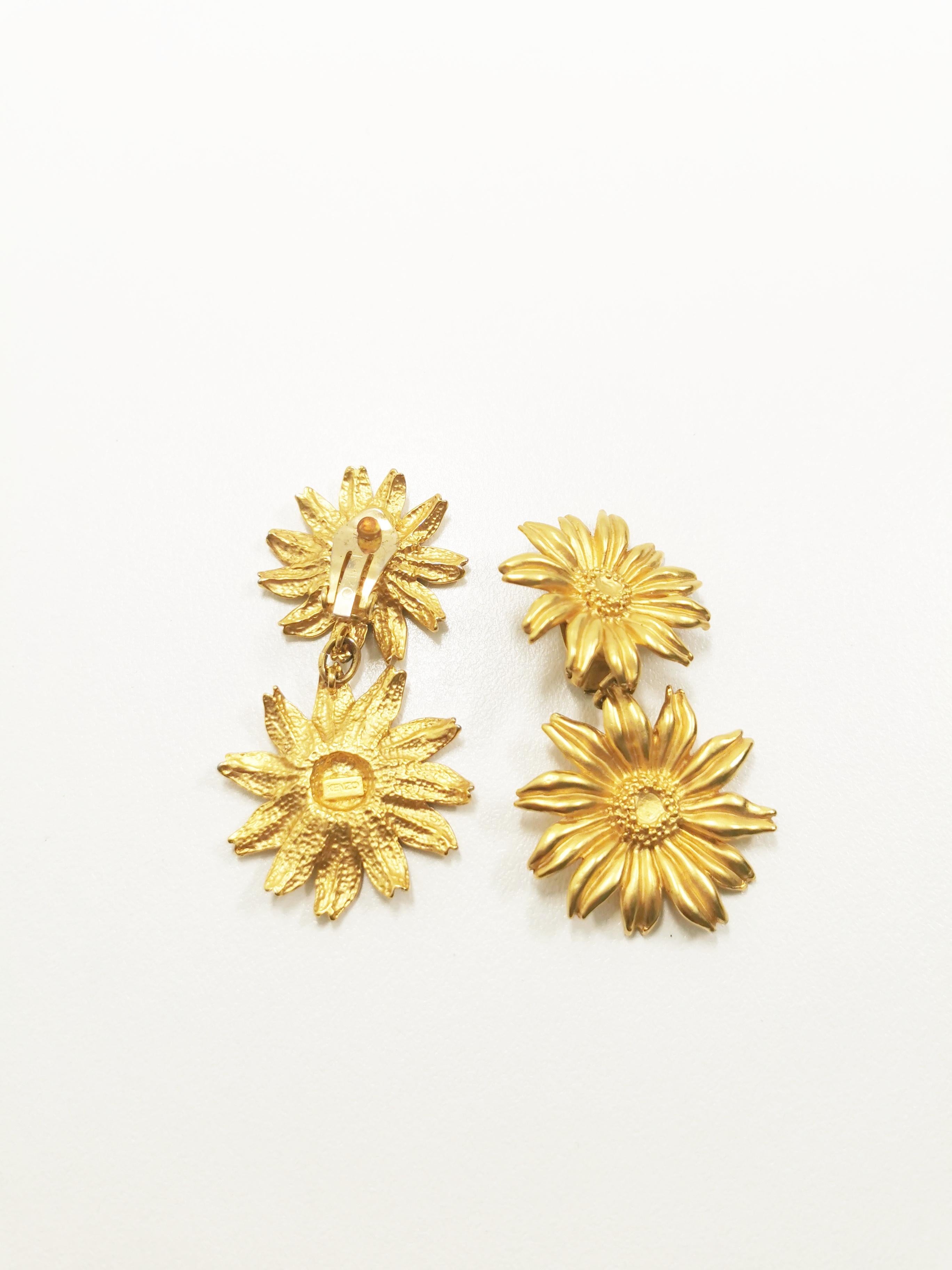Introducing the epitome of timeless elegance and bohemian charm, the Vintage KENZO Gerbera Flower Dangle Clip-On Gilded Earrings. Crafted with meticulous attention to detail, these exquisite earrings capture the essence of a bygone era, seamlessly