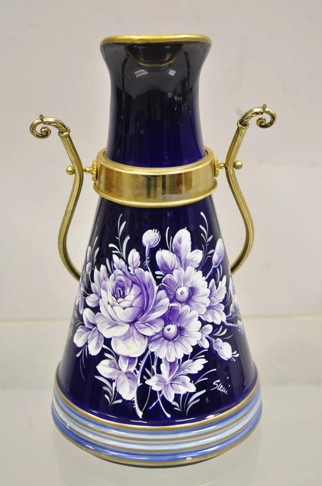 Vintage Keramos Italian Capodimonte Cobalt Blue Porcelain Pitcher w/ Handle. Item features purple painted flowers, brass reticulating handle, artist signature, original stamp.  Circa Late 20th Century. Measurements: 14.5