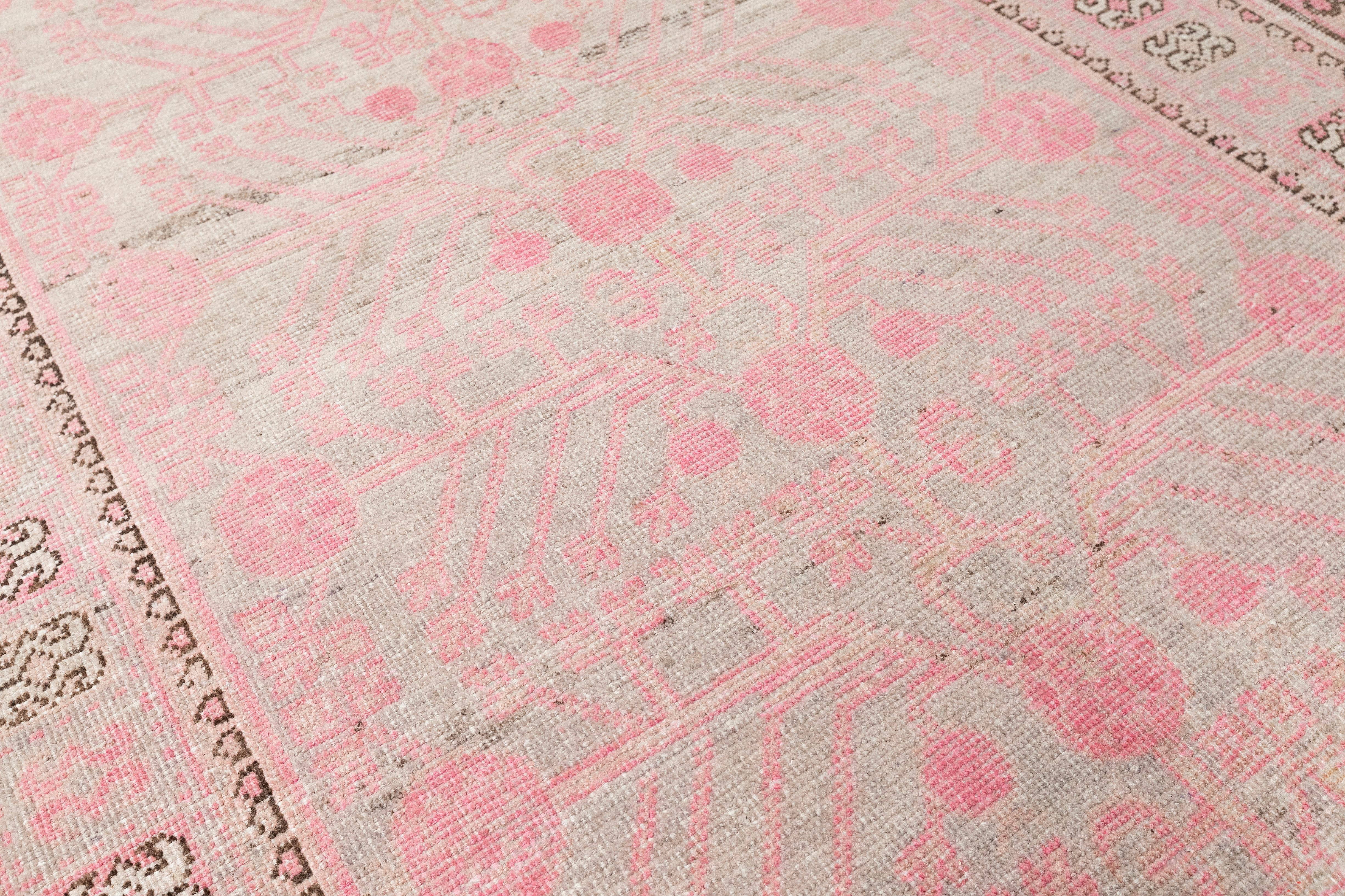 This vintage Khotan rug from Uzbekistan, approximately 70–80 years old, represents the finest traditions of Central Asian weaving. Handwoven by master artisans, it features a timeless geometric Khotan pattern rendered in naturally faded pink and