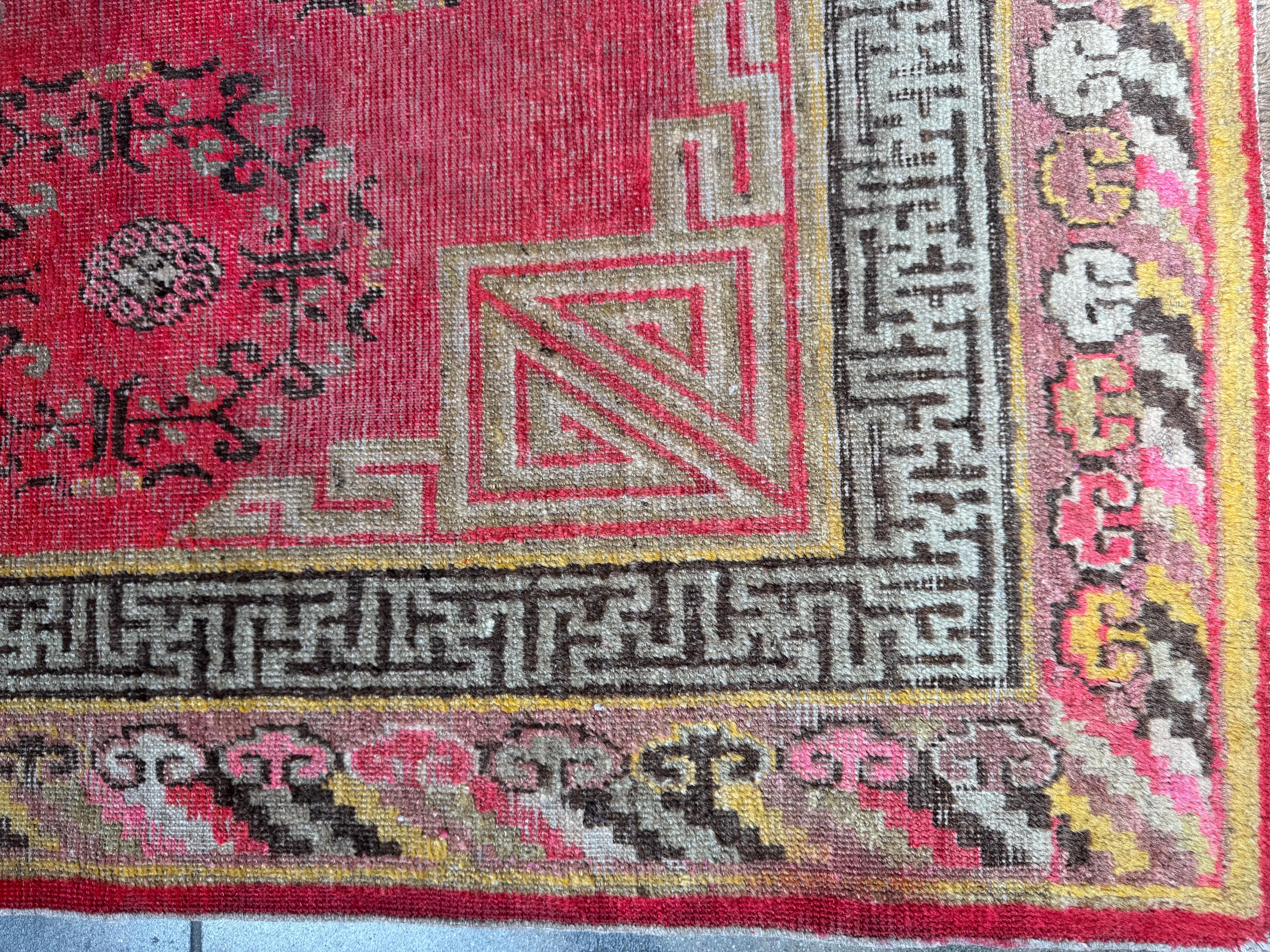 Dieser auffällige Vintage-Teppich aus Khotan-Samarkand zeigt ein kräftiges rotes Feld, das mit komplizierten Medaillonmotiven und traditionellen Mustern aus Ostturkestan verziert ist. Das symmetrische Arrangement, das von einer mehrschichtigen