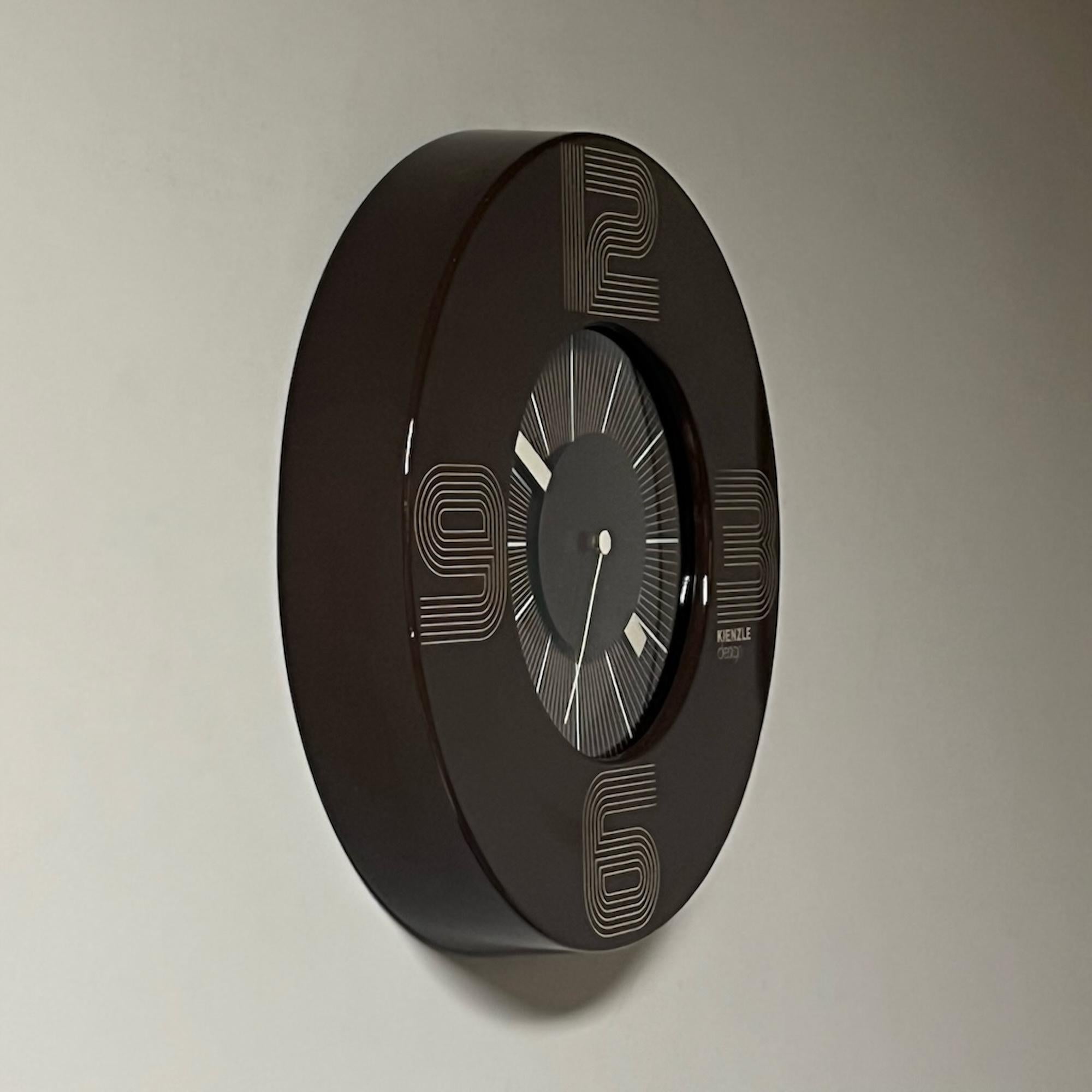 Amazing space age clock with a futuristic design made by Kienzle West Germany in the 1970s.

This unique vintage clock has a body made of lacquered brown metal that perfectly matches with the futuristic design of hours numbers and the distinctive