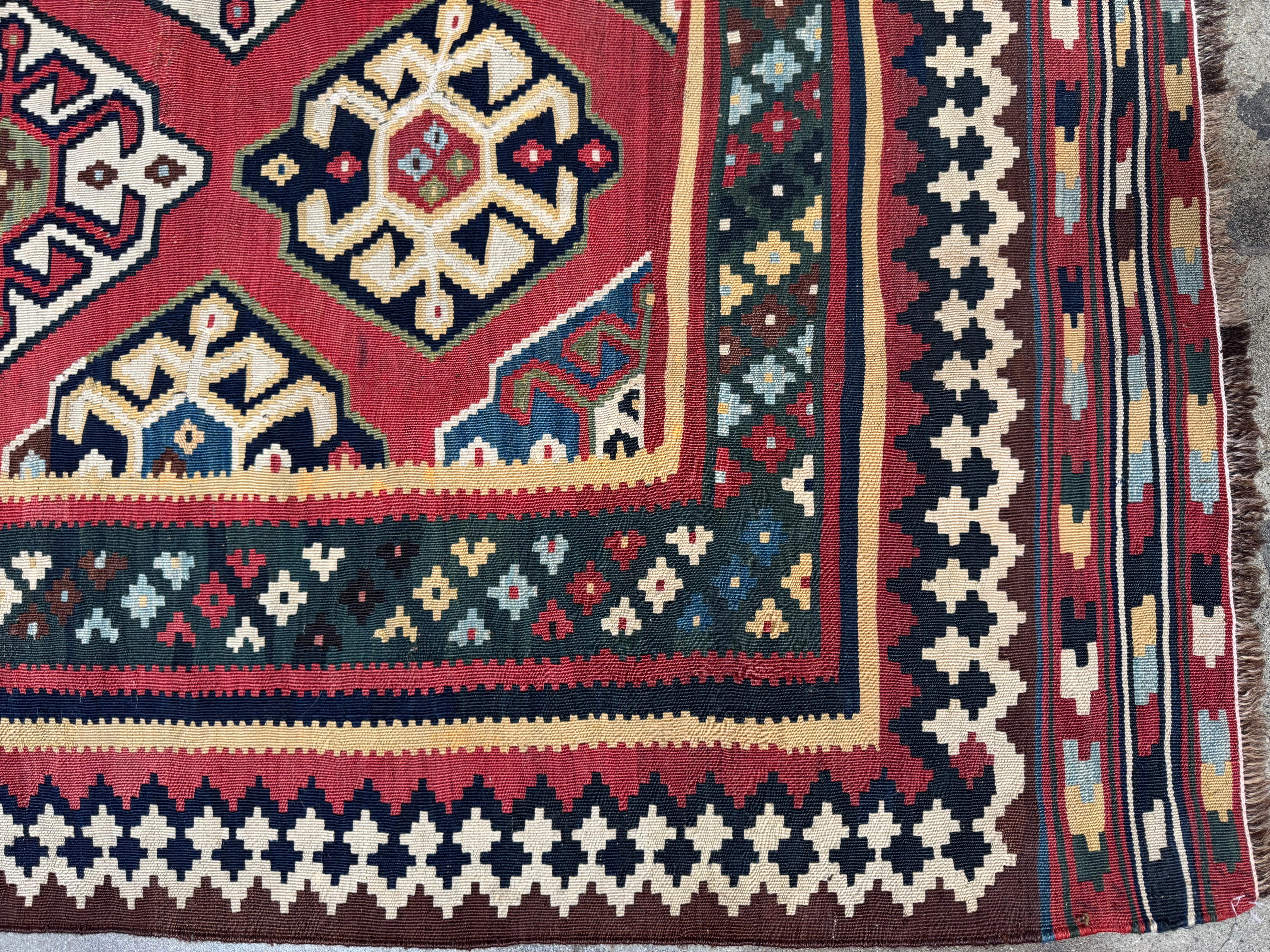 Dieser auffällige Vintage-Kilim-Ghashghai-Teppich zeigt ein kühnes und lebhaftes Stammesmuster, handgewebt mit geometrischen Rautenmotiven in einer fesselnden Farbpalette aus Rot, Elfenbein, Grün und Indigo. Dieses von den nomadischen