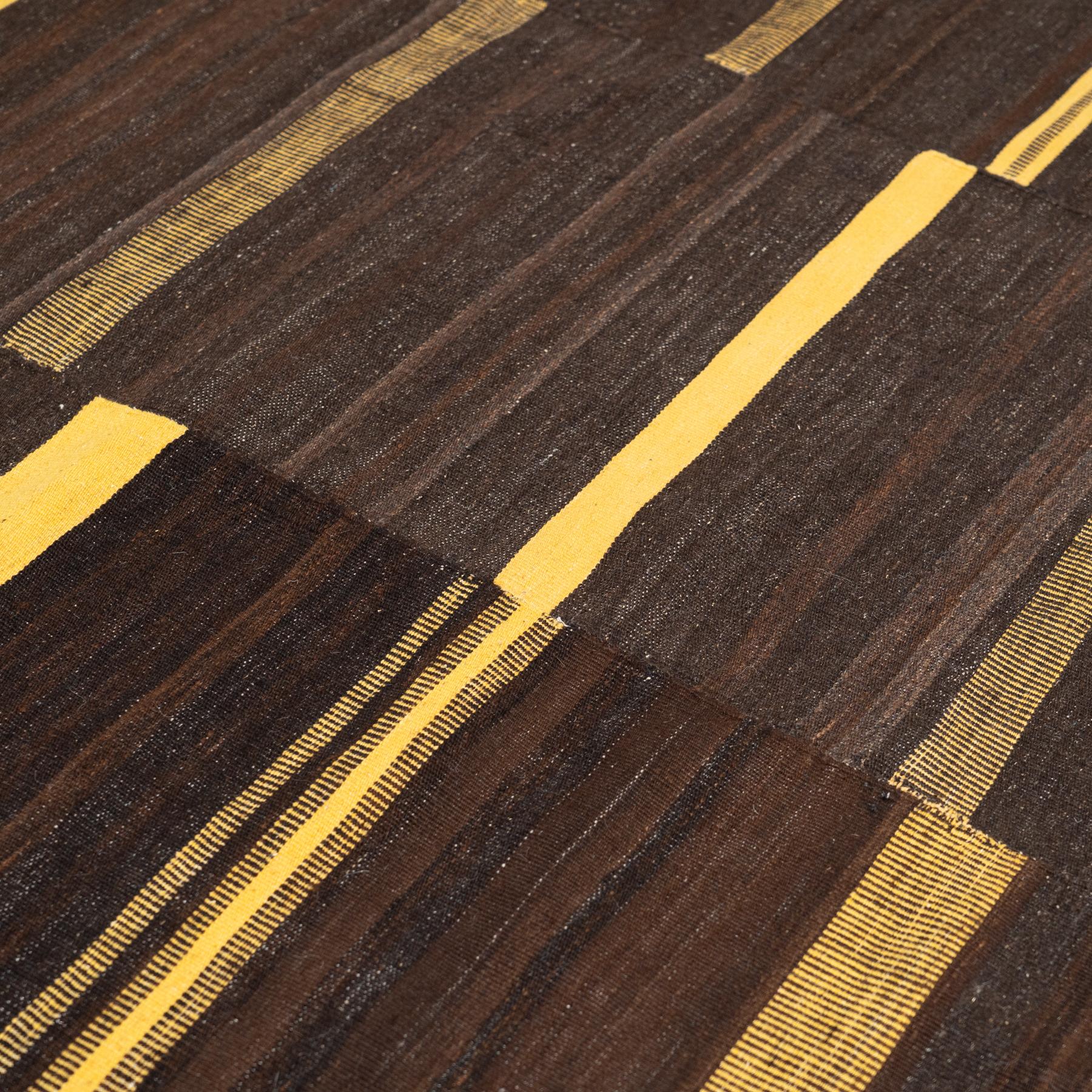 This vintage Kilim rug, handwoven around the 2000s, combines the warmth of earthy brown and yellow tones with a modern, minimalist design inspired by the Bauhaus movement of the early 20th century. Measuring 178 x 241 cm, this striking rug is the