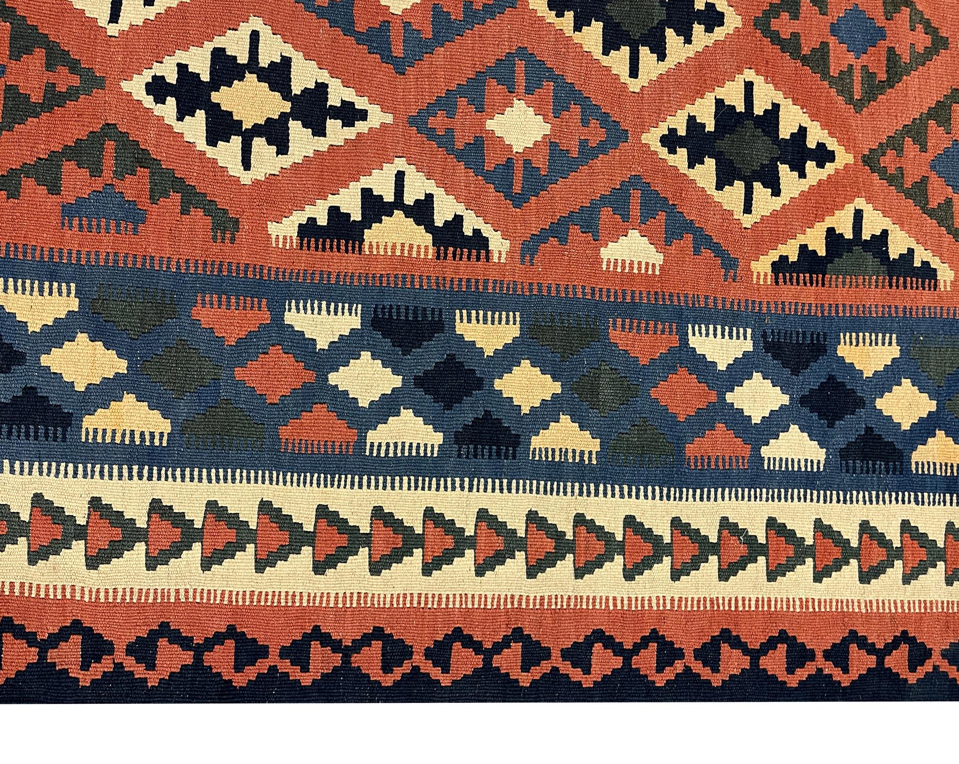 This fine kilims wool area rug is an excellent example of flat-woven area rugs woven in the late 20th century, circa 1980. The design features an orange background kilim rug with geometric motifs woven in beige, green, blue and cream accents.