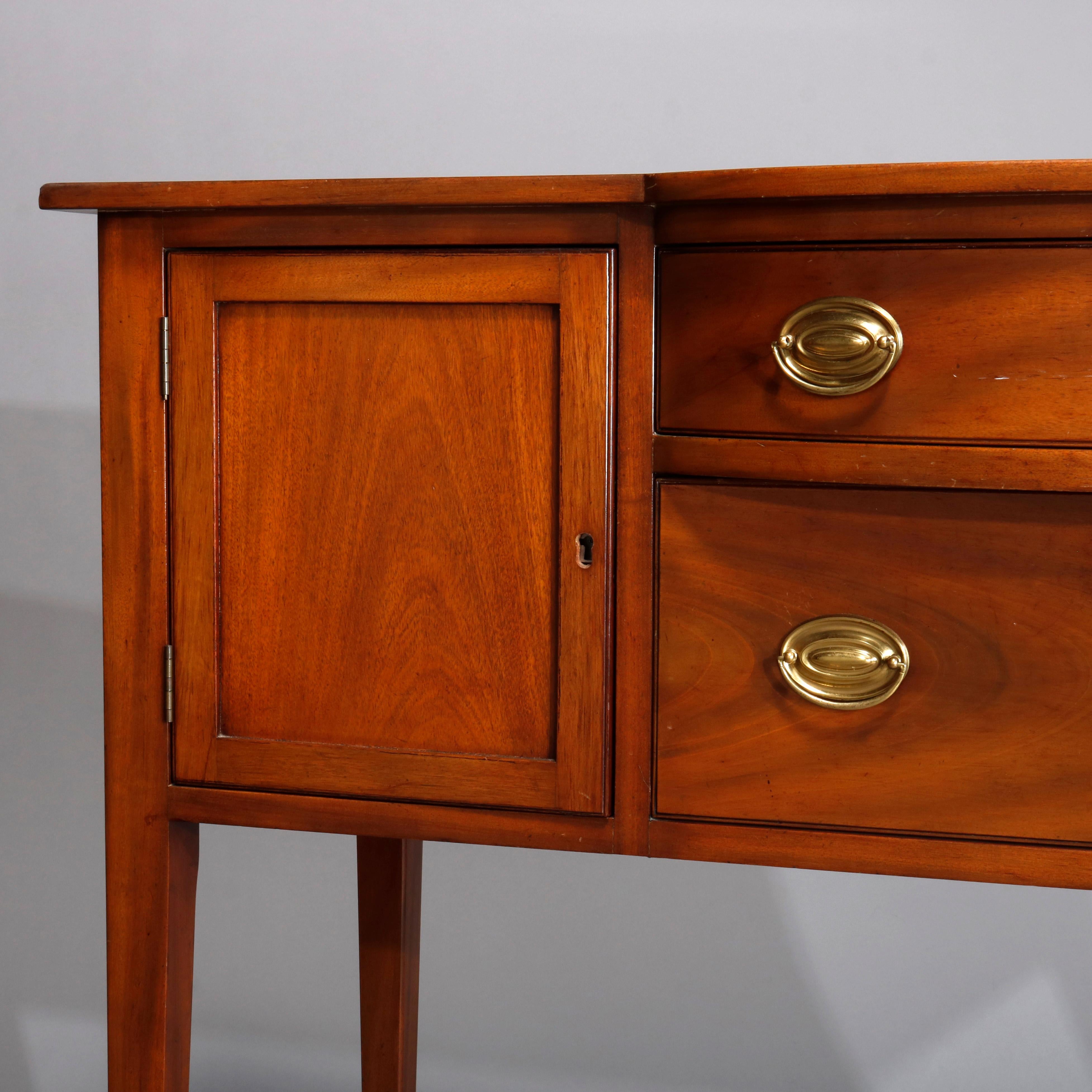 A vintage sideboard by Kittinger of the Williamsburg Adaptation line offers mahogany construction with shaped top surmounting central stacked drawers having flanking cabinets with paneled doors, raised on square and tapered legs, maker label and