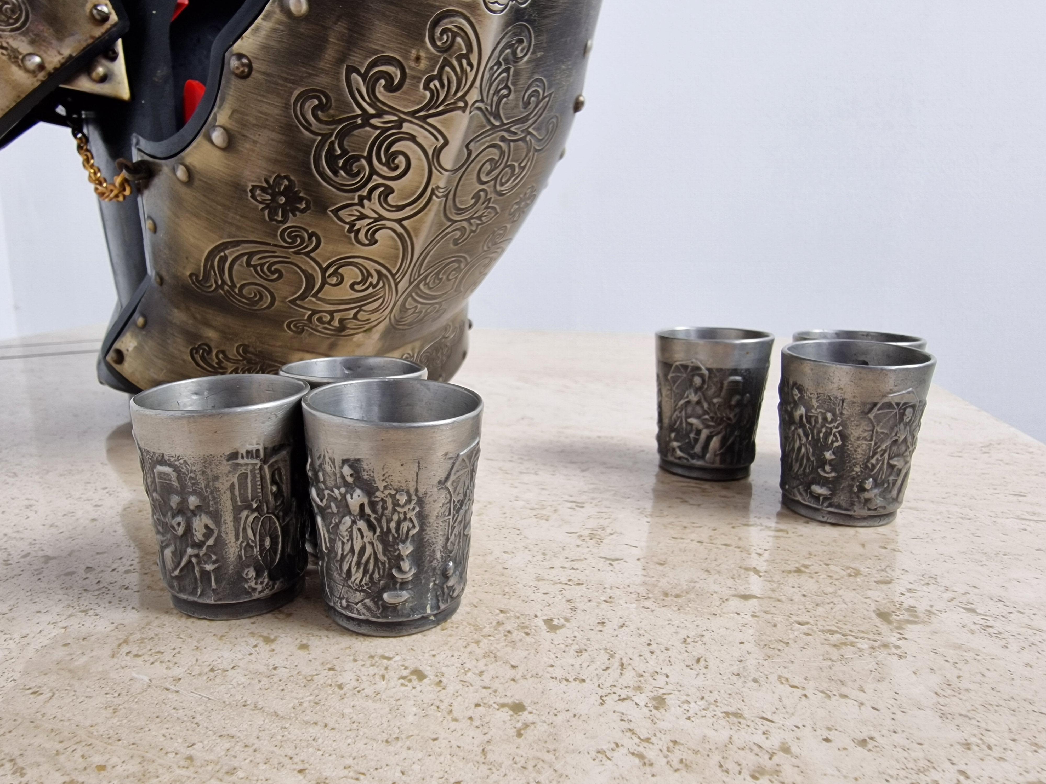 This is a rare and unusual, detailed and well-produced bar set containing 6 shot glasses and a bottle, all within a stand modeled as the upper body of a Medieval knight.

The front has an ornately scrolled metal breast plate which pulls down like