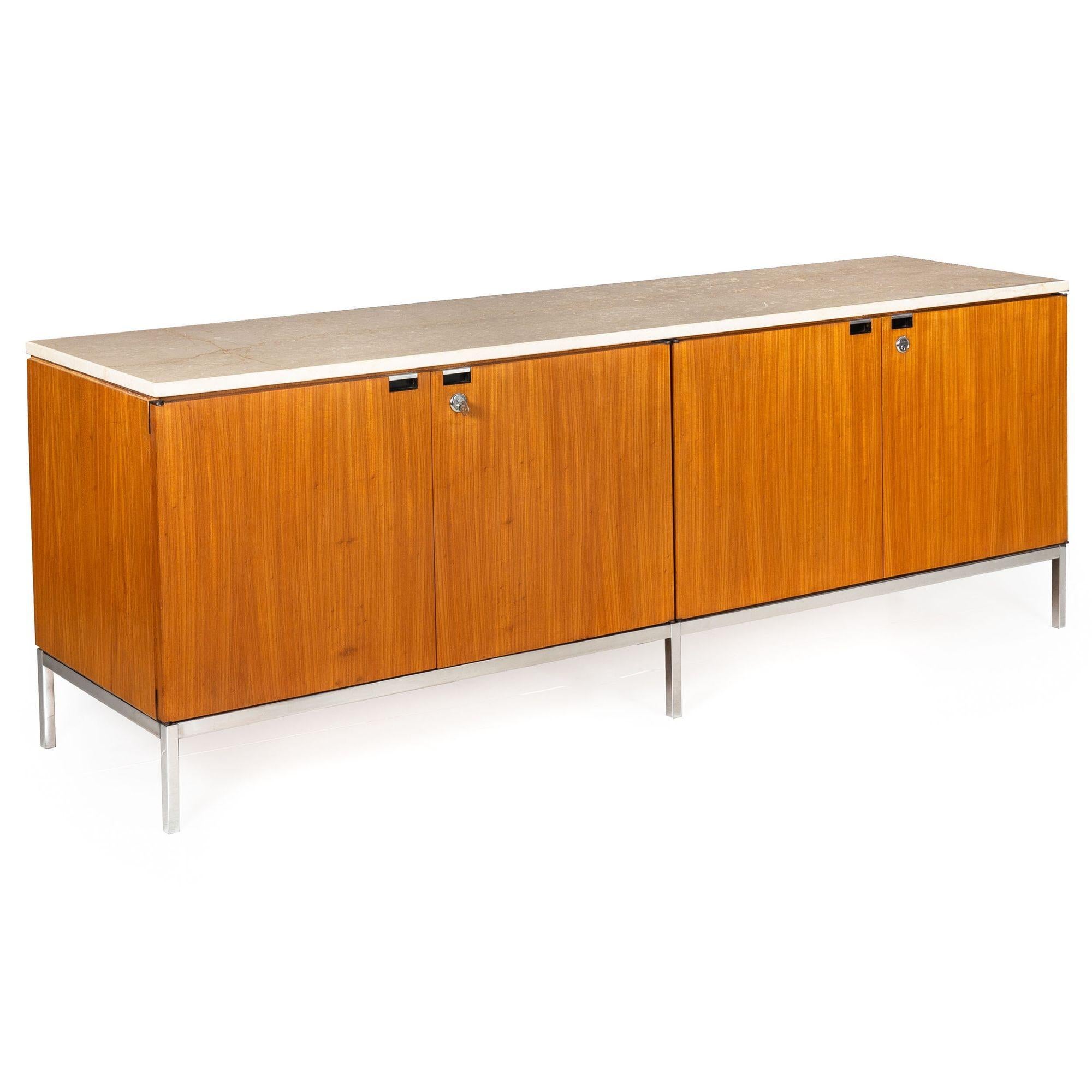 A very nice double-credenza designed and retailed by Knoll, it features a polished marble top (with repaired crack) over an all-over teak facade raised on polished chrome legs. The doors open to reveal a shelved interior. Versions of this cabinet