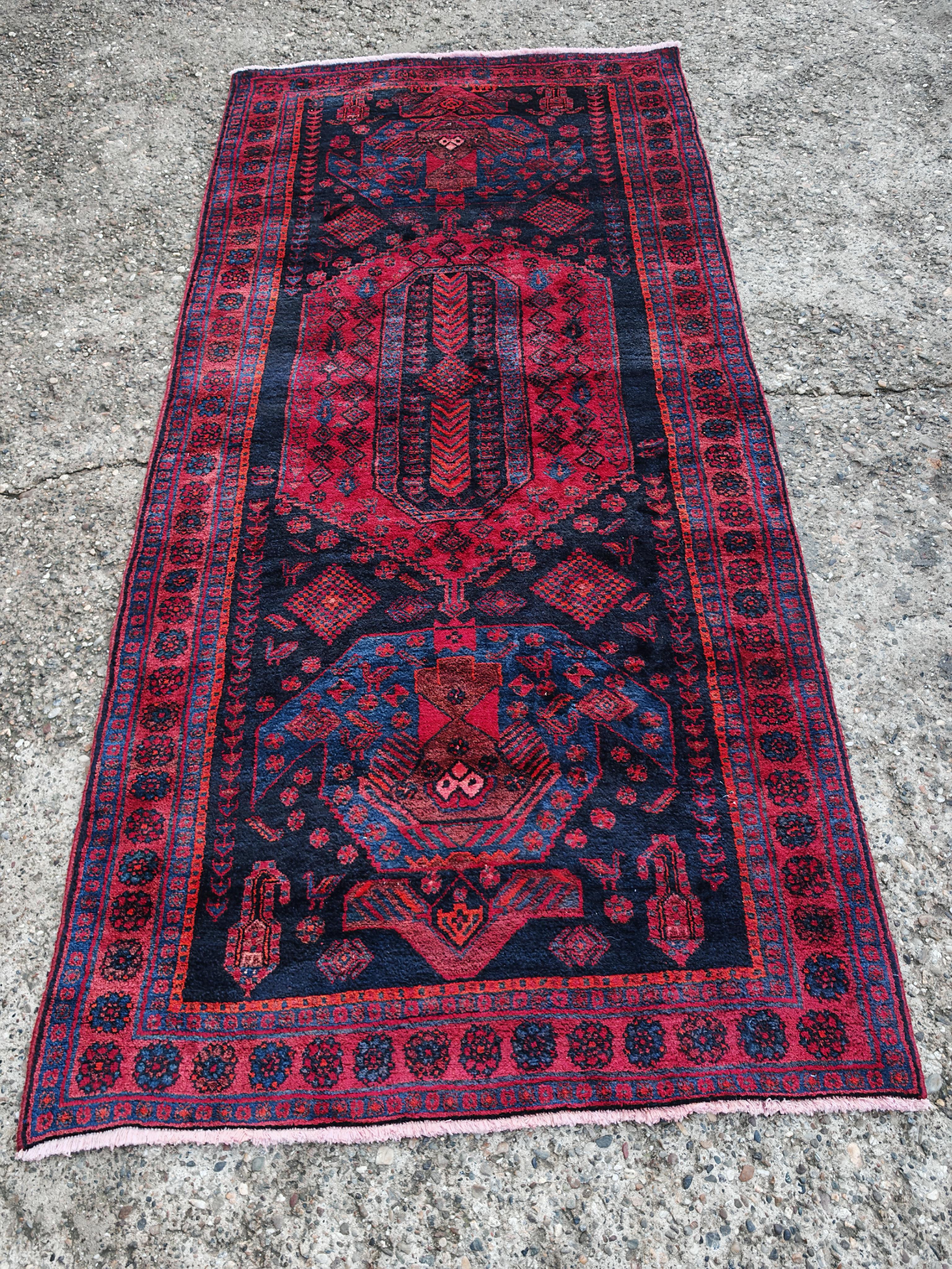 In this listing you will find a stunning vintage Kolyai rug. The rug is hand-woven, with the dominant colors of rich, dark shades of red and navy blue, often highlighted with black outlines and touches of white or ivory. The design is geometric and