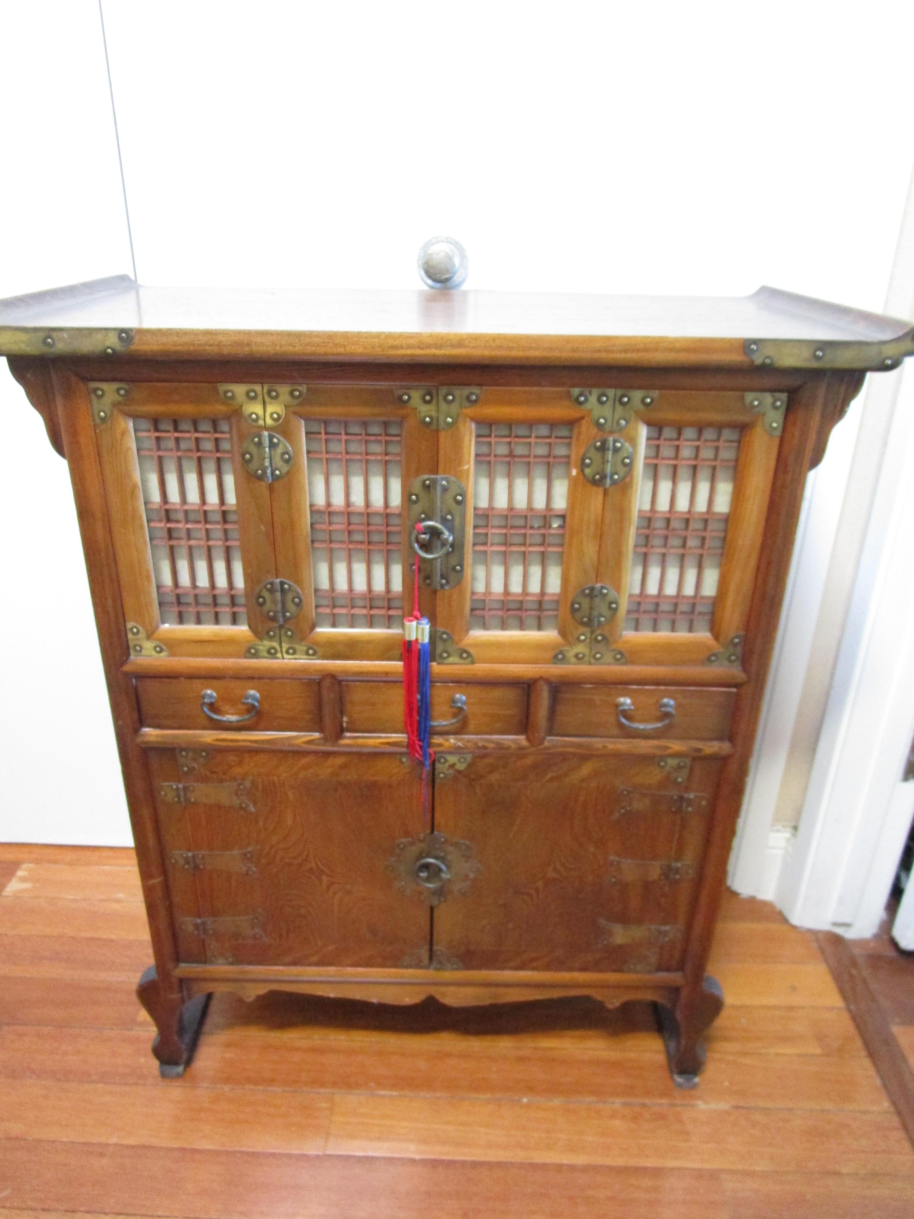 This is a beautiful Korean elm storage cabinet with drawers and wonderful details. The wood has a lovely deep patina. The cabinet has elements all over in brass including the hinges. The top has the familiar up-scrolled ends and the four doors at
