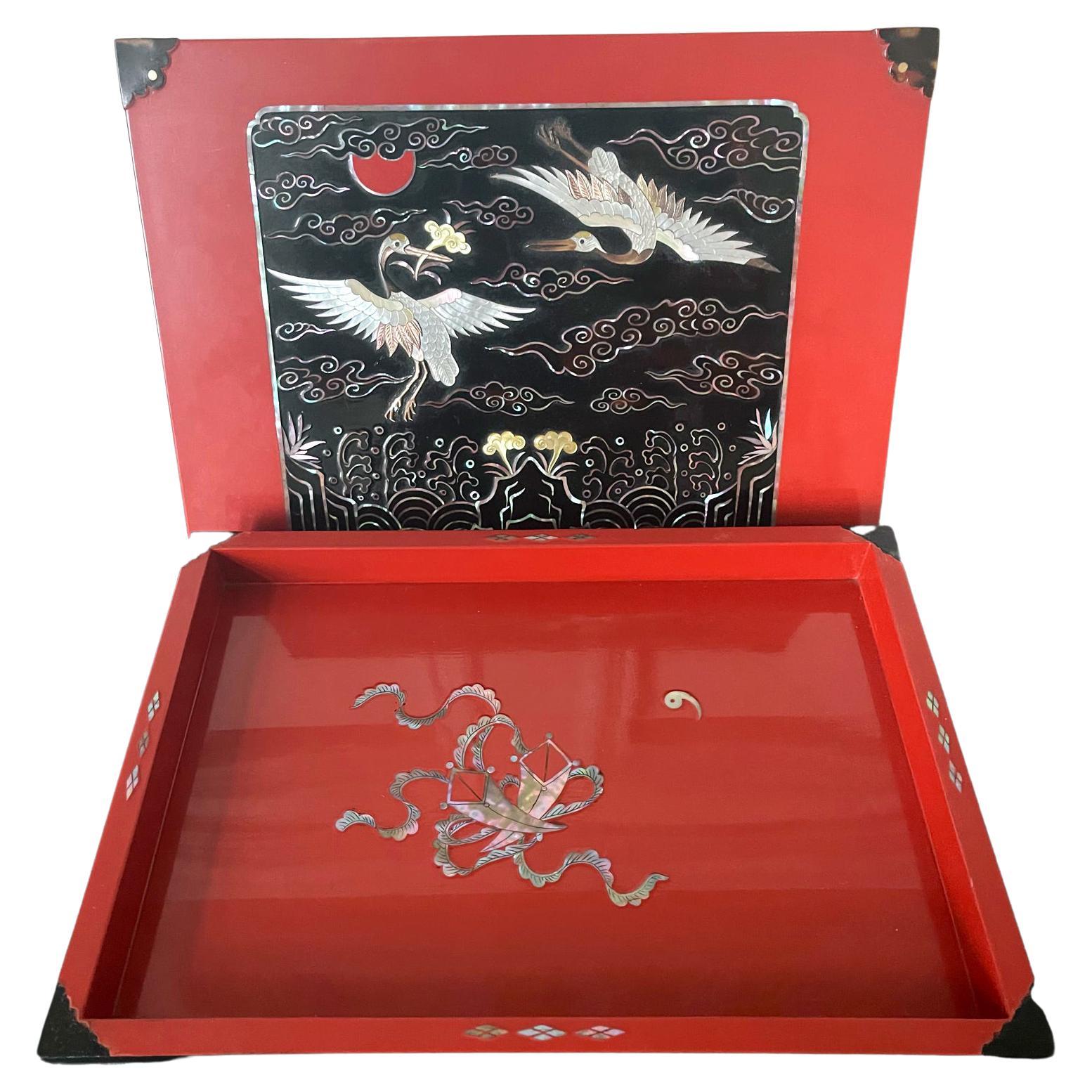 A lovely vintage Korean lacquer box in bright red and decorated with mother-of-pearl inlays circa 1970-80s. The square form box features an auspiciously rendered panel on the top surface of the lid. Within the black rectangular field, MOP inlays was