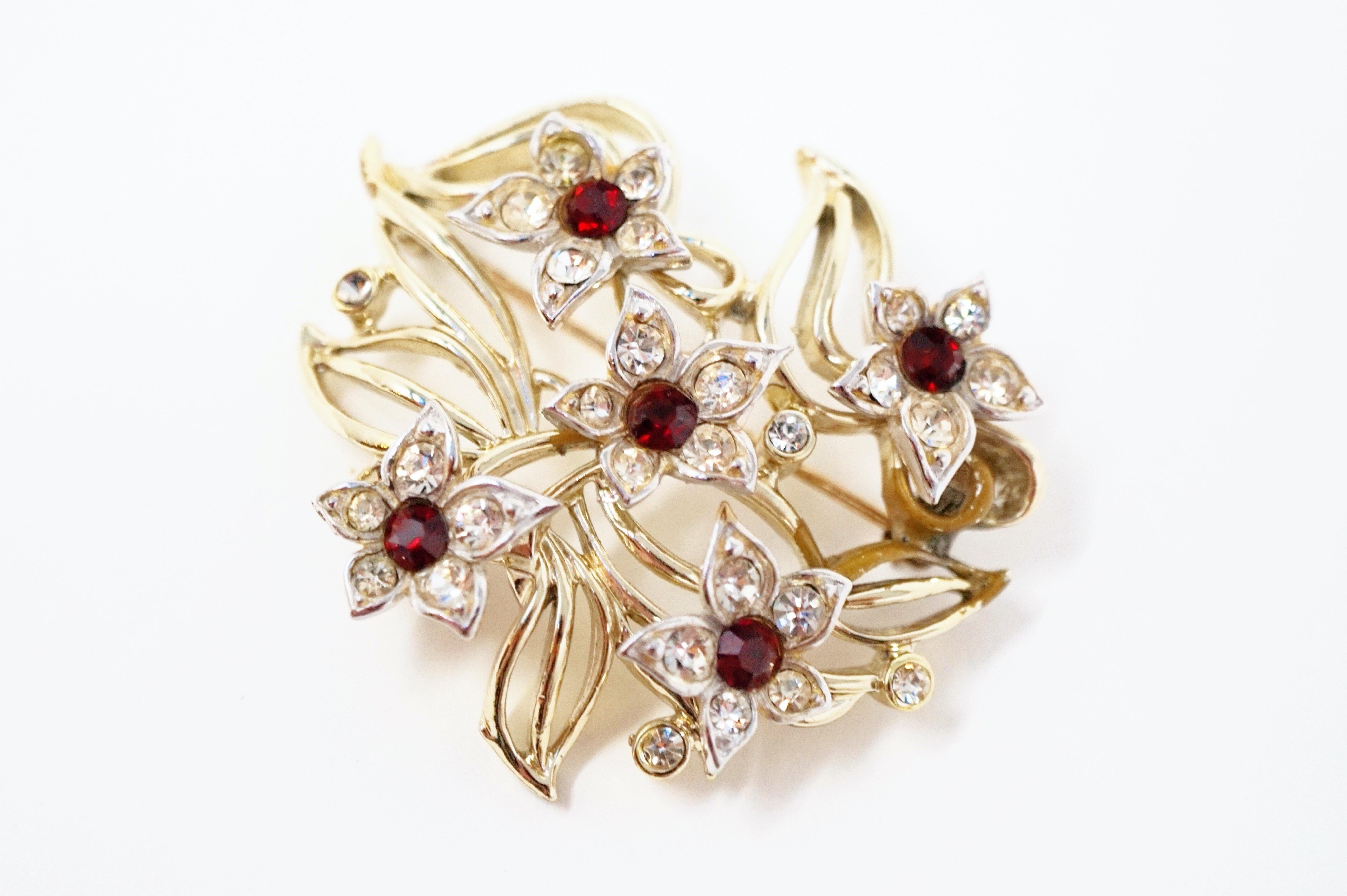 This beautiful vintage floral figural brooch is by iconic costume jewelry brand Kramer Jewelry, circa 1950s. Five silver tone flowers adorn this piece, with clear crystal rhinestones on each petal and a ruby red colored crystal rhinestone in the