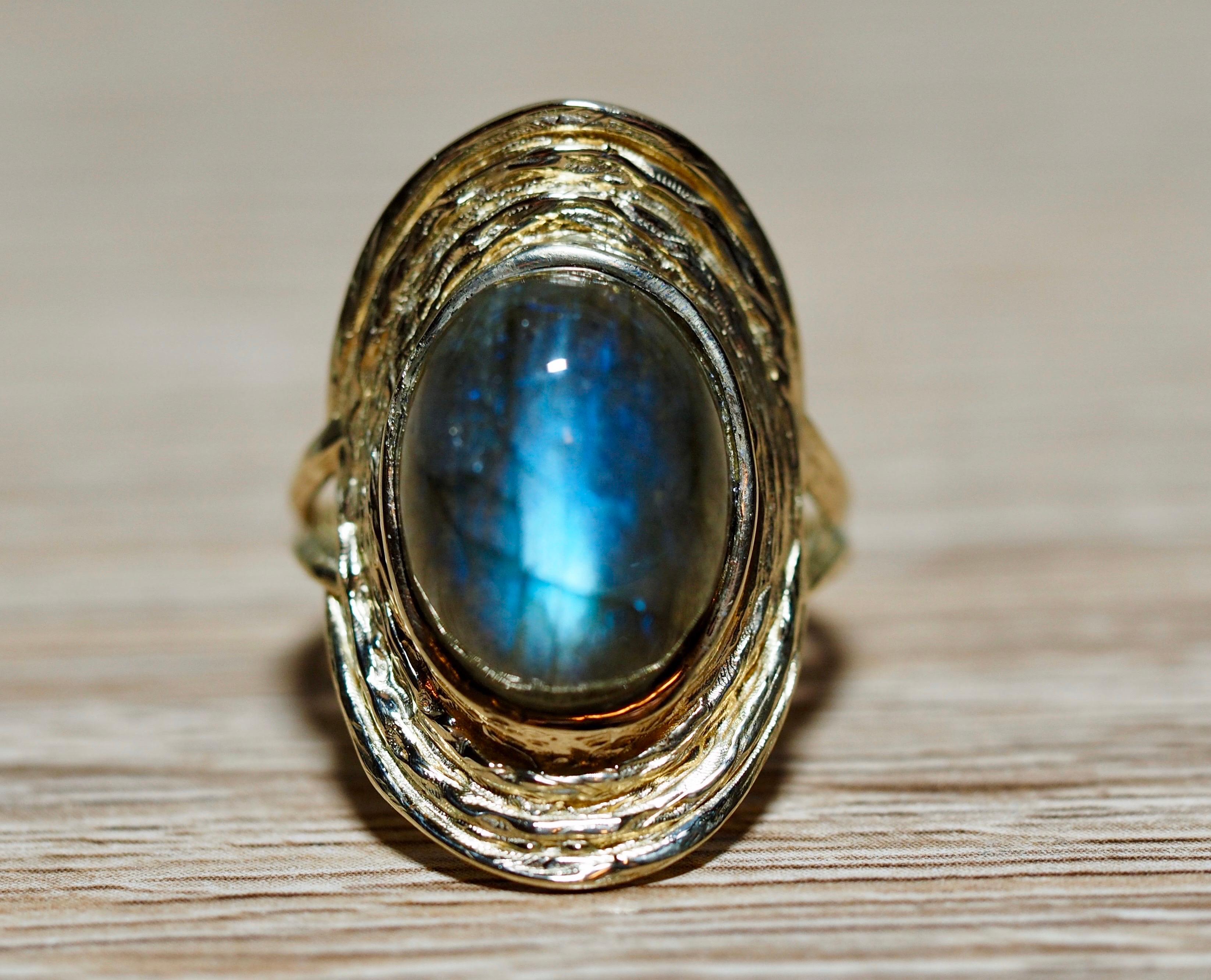 Vintage 14- Karat yellow gold ring is glowing with a 9.10 carat labradorite cabochon  oval center. The majestic center is glowing in hues of blues and soft touches of purple that glisten as it touches the light. It is bezel set in a frame of 14