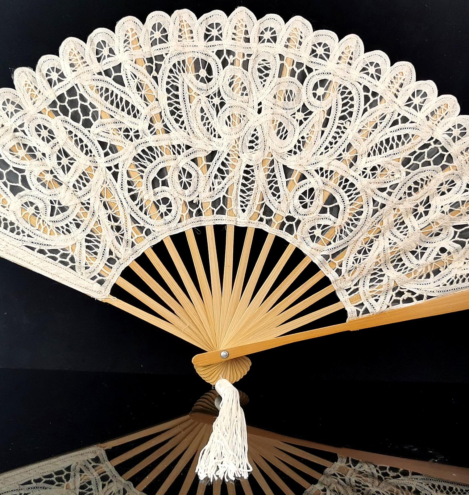A large vintage lace and wood hand fan.

It is made from machine lace in an antique applique lace design in a rich cream colour and affixed to light tone hardwood sticks and guards with a small silky polyester tassle to the base.

It is a good sized