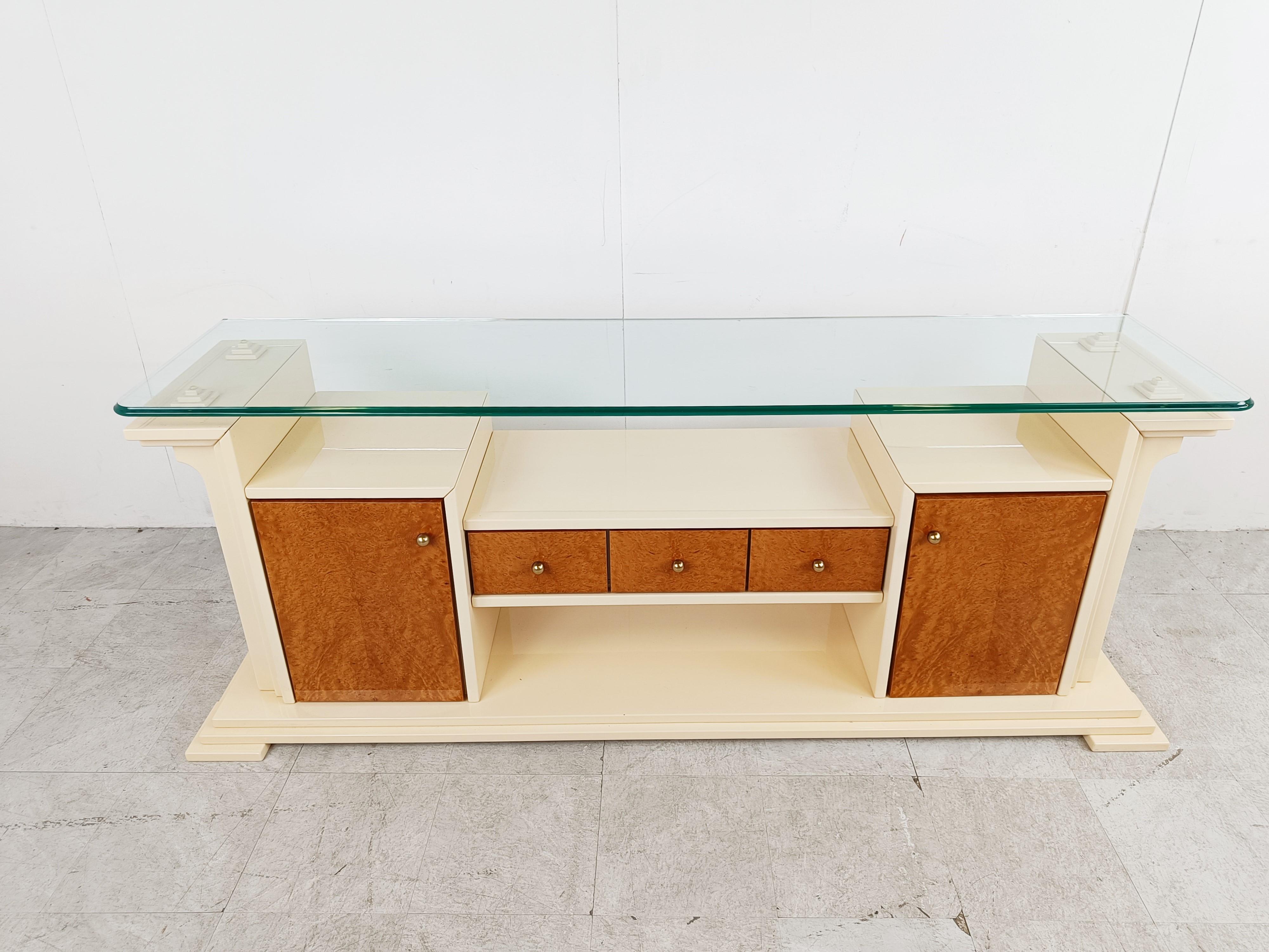 Luxurious 1980s sideboard made from beige lacquered wood with burl wood doors and drawers and brass handles. 

The sideboard has a glass top.

Striking architectural design.

1980s - France

Dimensions:
Lenght: 195cm/76.77