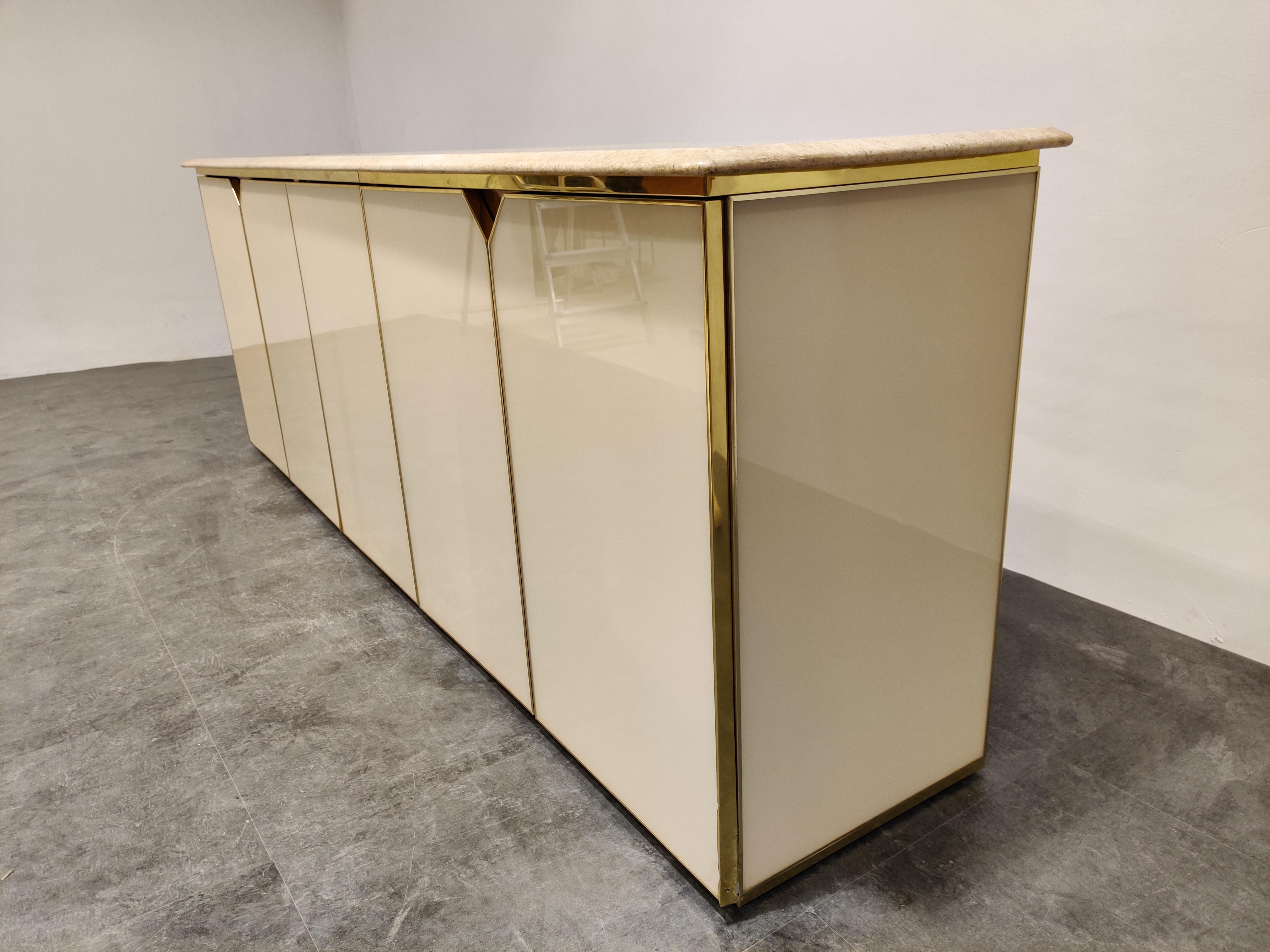 Luxurious brass lacquered credenza with a beautiful travertine stone top.

The doors have a brass finish, giving the cabinet a luxurious appeal.

The credenza consists of five doors and offer enough storage space.

Good overall condition, the