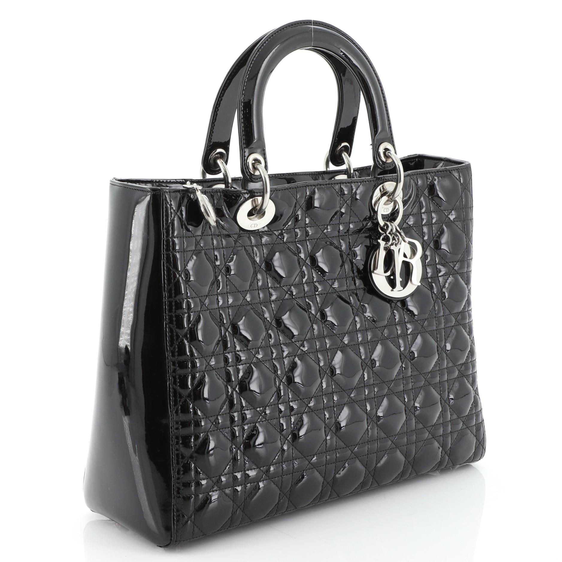 This Christian Dior Vintage Lady Dior Bag Cannage Quilt Patent Large, crafted from black patent leather in Dior's iconic cannage quilting, features dual-rolled handles with sleek Dior charms, protective base studs, and silver-tone hardware. Its top