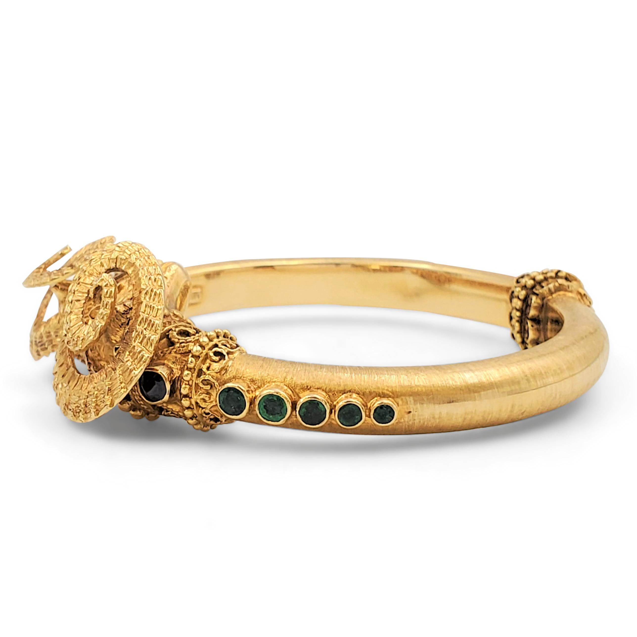 Authentic Ilias Lalaounis hinged bangle bracelet crafted in 18 karat yellow gold. A silky florentine finish contrasts with handcrafted textured detail and beadwork. The design is accented by bezel-set emerald, sapphire, and ruby stones. Signed Ilias