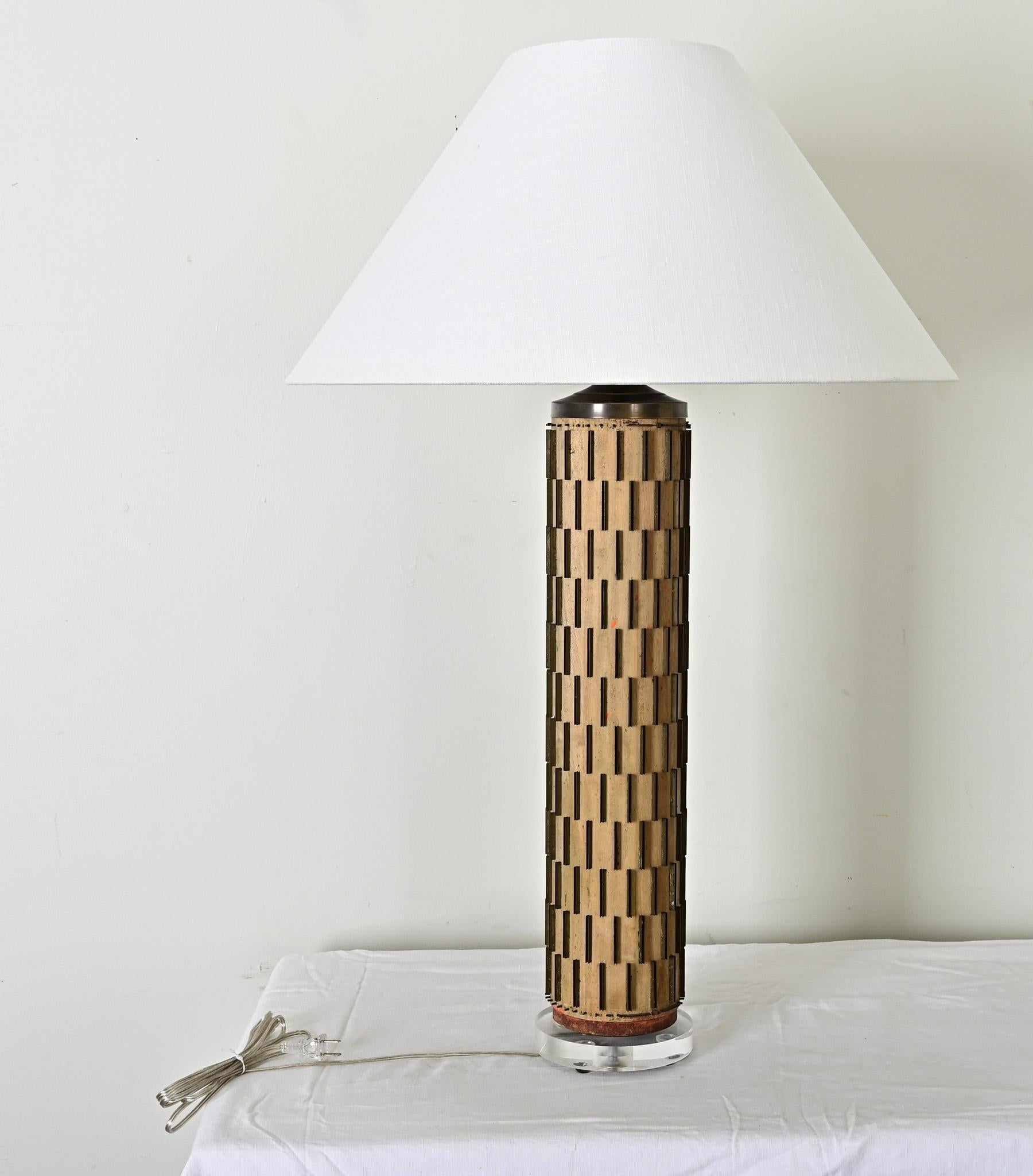 Un magnifique rouleau d'encre de papier peint vintage réutilisé - ou upcyclé - pour en faire une lampe de table. Surmonté d'un nouvel abat-jour conique en lin blanc, le cylindre de bois est armé de rangées de lames métalliques qui apportent