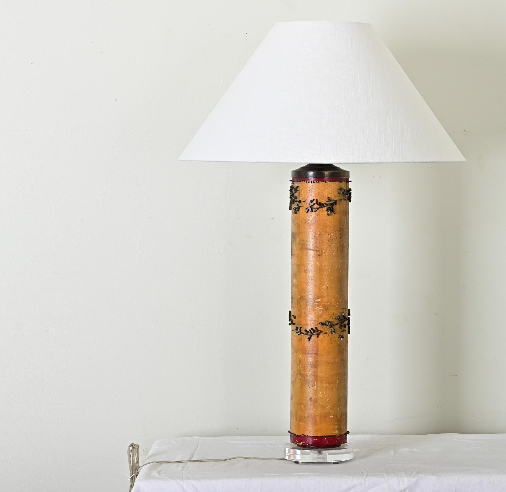 Un magnifique rouleau d'encre de papier peint vintage réutilisé - ou upcyclé - pour en faire une lampe de table. Surmonté d'un nouvel abat-jour conique en lin blanc, le cylindre est ponctué par ce qui reste du tampon en laiton à fleurs et à