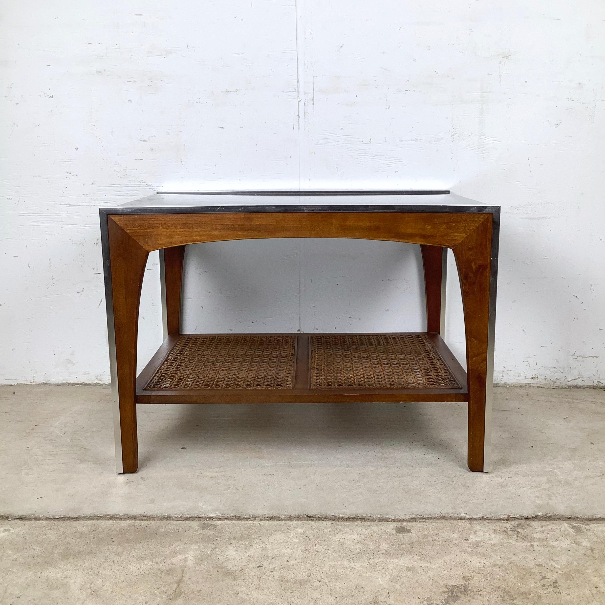 This vintage Lane end table blends the best elements of mid-century design—glass, wood, metal, and woven cane—into one strikingly cohesive piece. Its smoked glass top creates a sleek, modern surface that instantly draws the eye. Beneath it, the cane