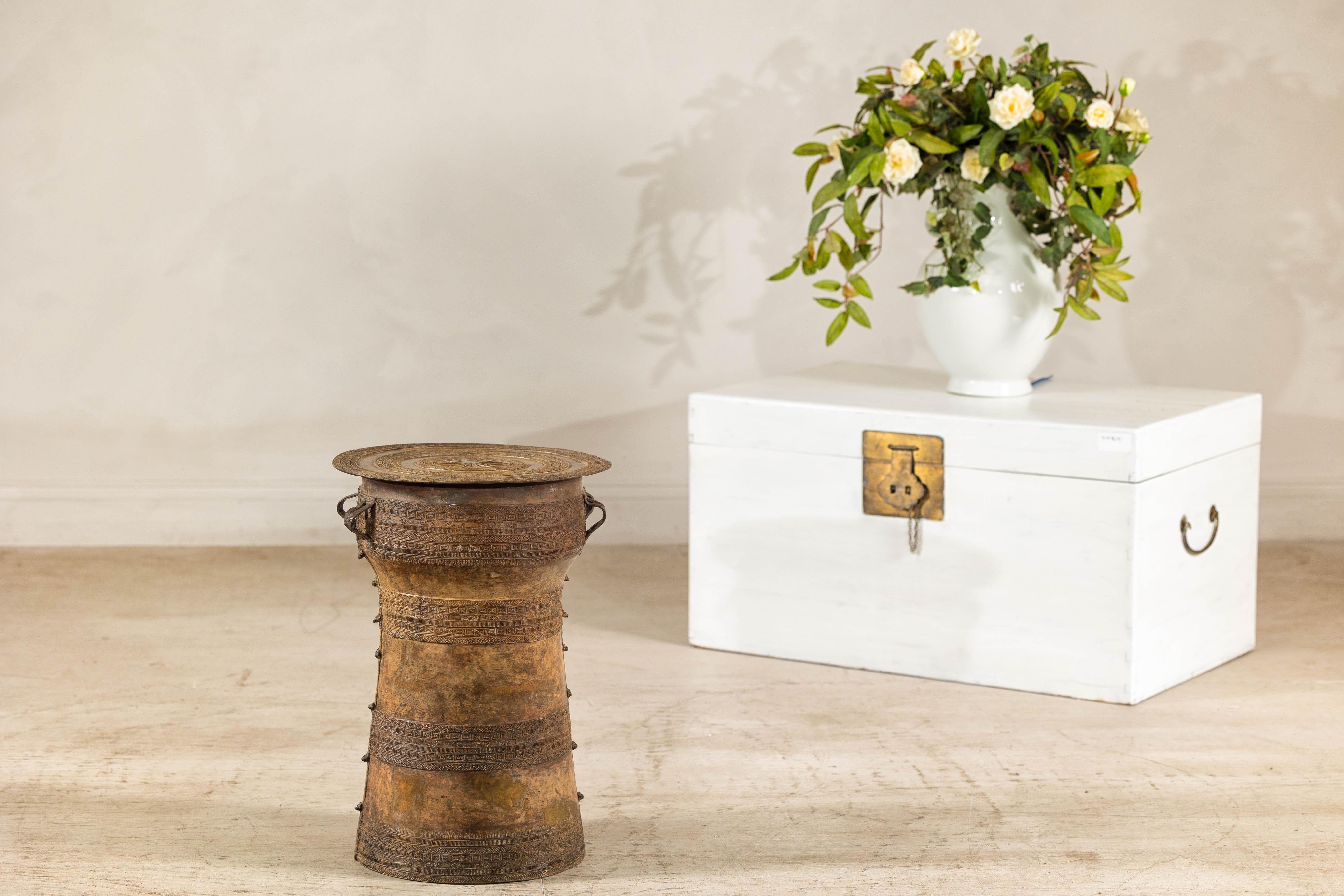 A vintage cast bronze Laotian style rain drum table with antique gold patina. This vintage cast bronze Laotian-inspired rain drum table brings an exotic touch to any space. The table features a beautifully detailed cylindrical body adorned with