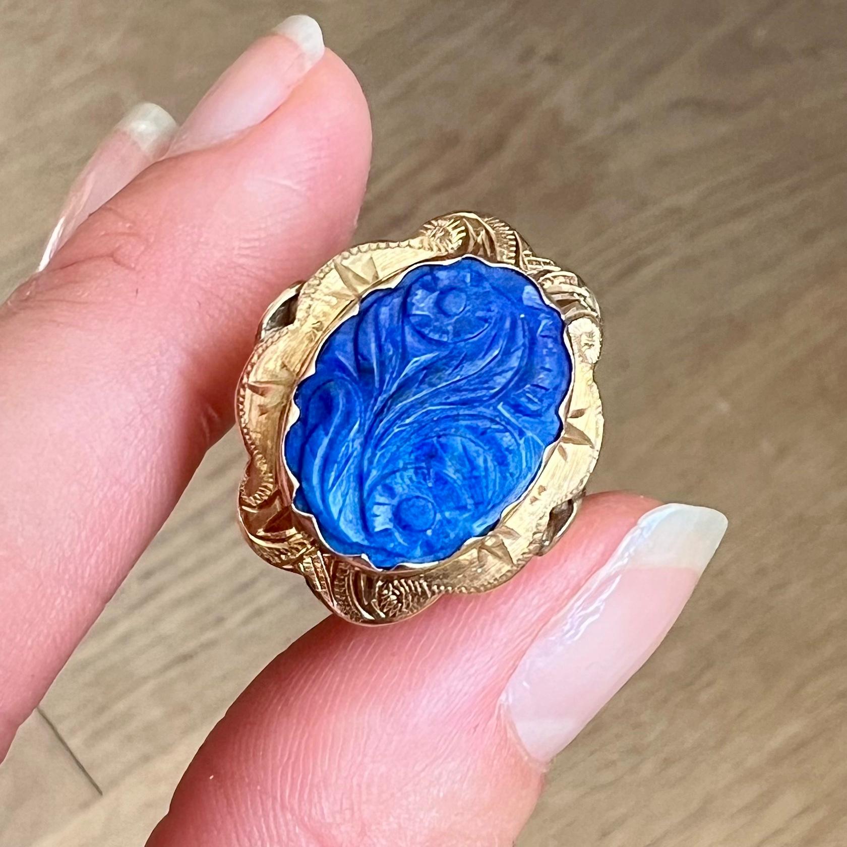 This is a vintage 14 karat yellow gold ring crafted with a beautiful carved lapis lazuli gemstone. The design creates this lovely engraved gold mounting of the ring. The edge of the mounting is oval-shaped and scalloped. The lapis has an amazing