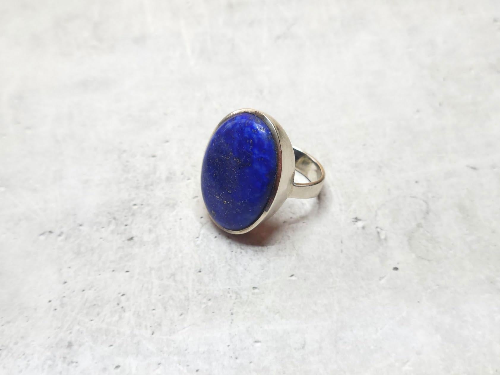 This elegant and comfortable ring showcases a beautifully polished lapis lazuli cabochon, securely set in a classic sterling silver band. The deep blue hues of the natural lapis lazuli, with its characteristic golden flecks, create a striking