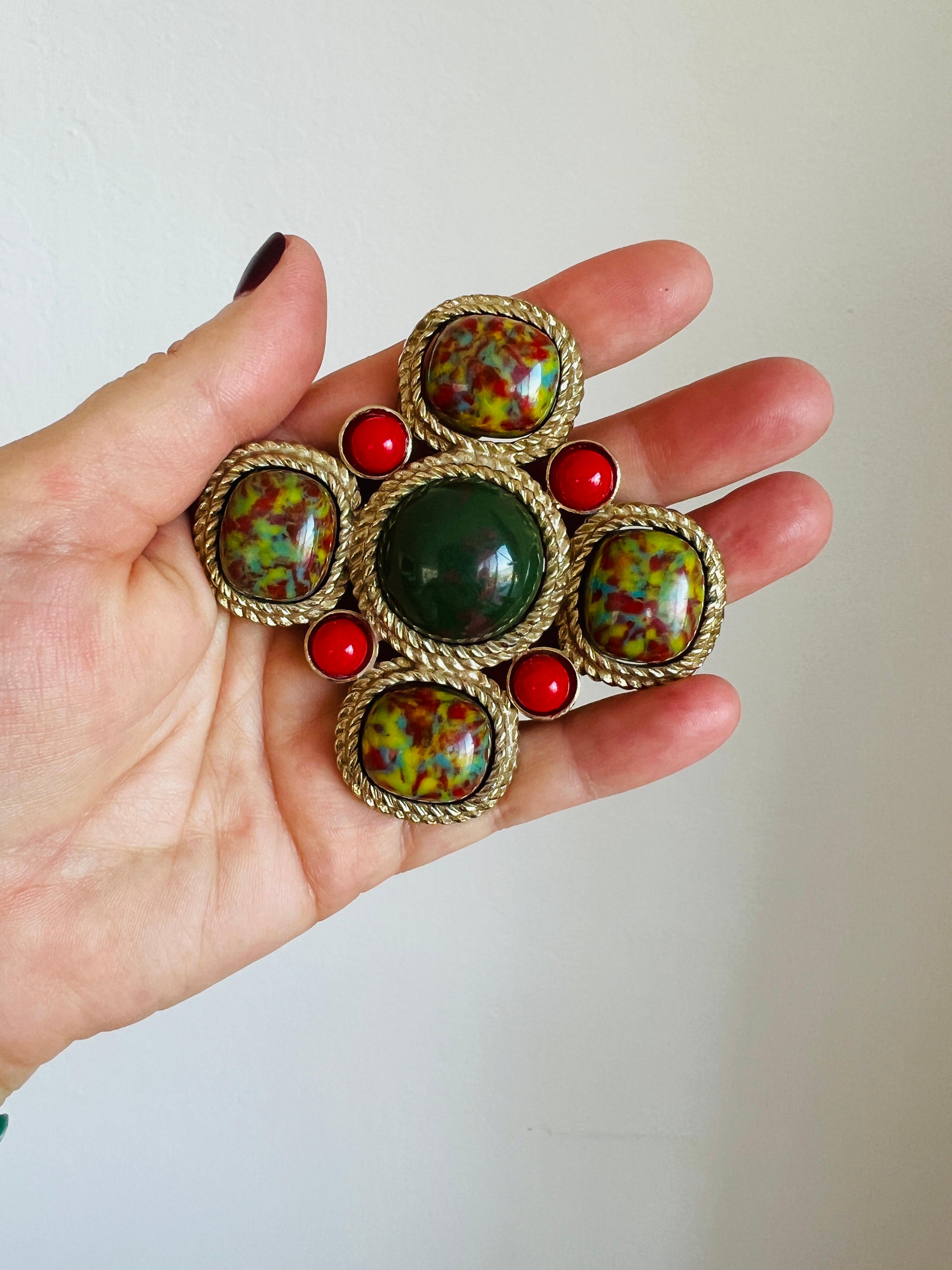 This striking vintage Maltese cross brooch by Sarah Coventry exudes bold sophistication. Its richly marbled cabochons in green, yellow, and red, paired with deep red accent stones, create a vibrant palette reminiscent of regal Byzantine design. The